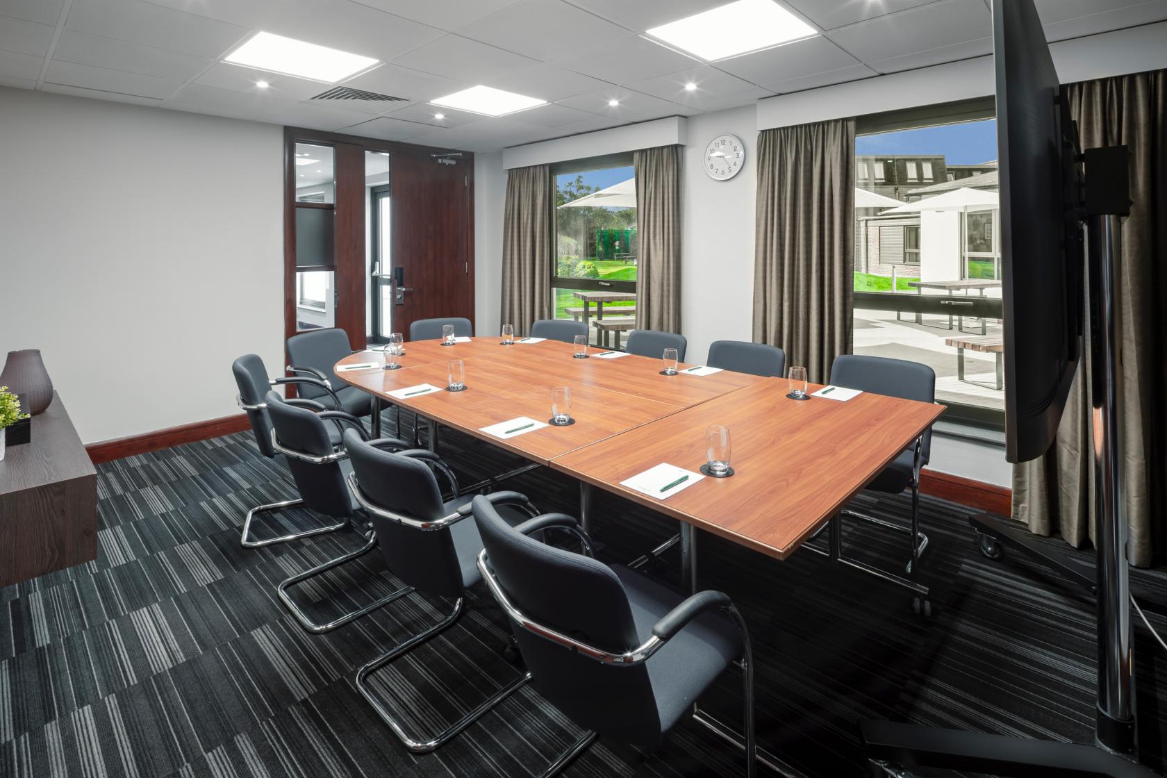 A boardroom with a rectangular wooden table, black chairs, and large windows at Holiday Inn London Bexley.