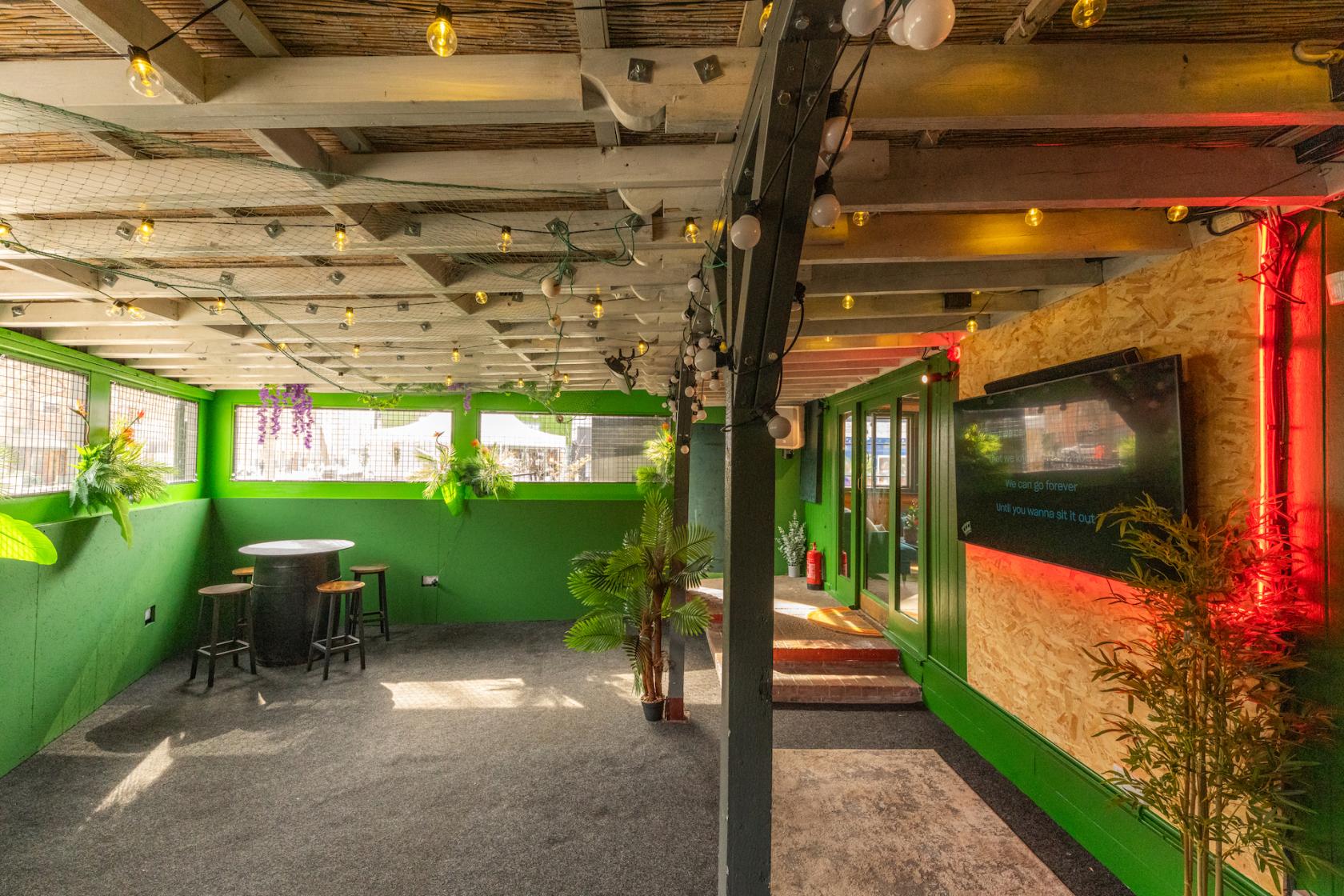 A lounge with string lights, green painted walls, potted plants, and a high-top table at LIMIN SOUTHBANK.