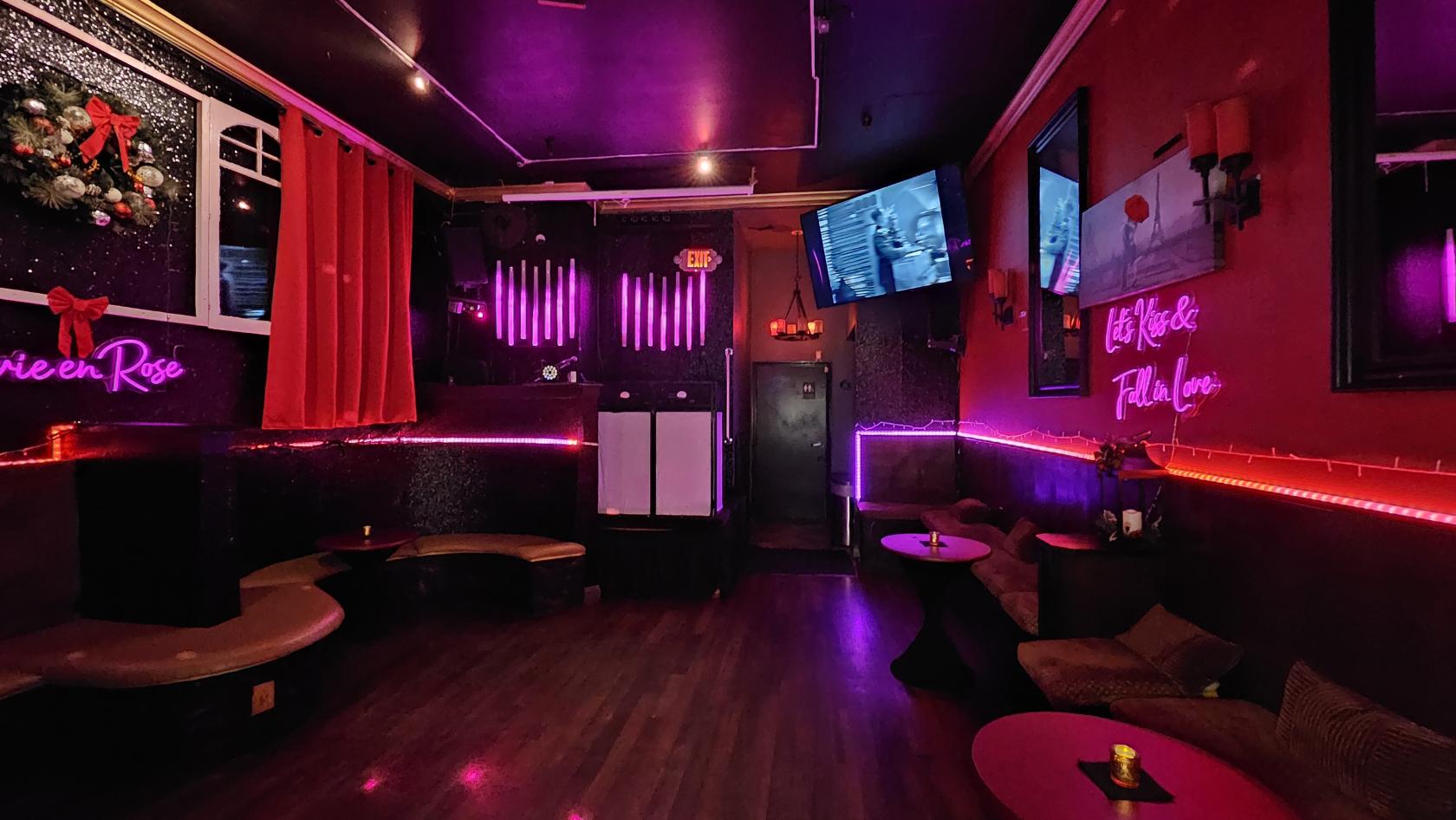 A cocktail lounge with neon pink lighting, wall-mounted TVs, and curved seating at Paris 75.