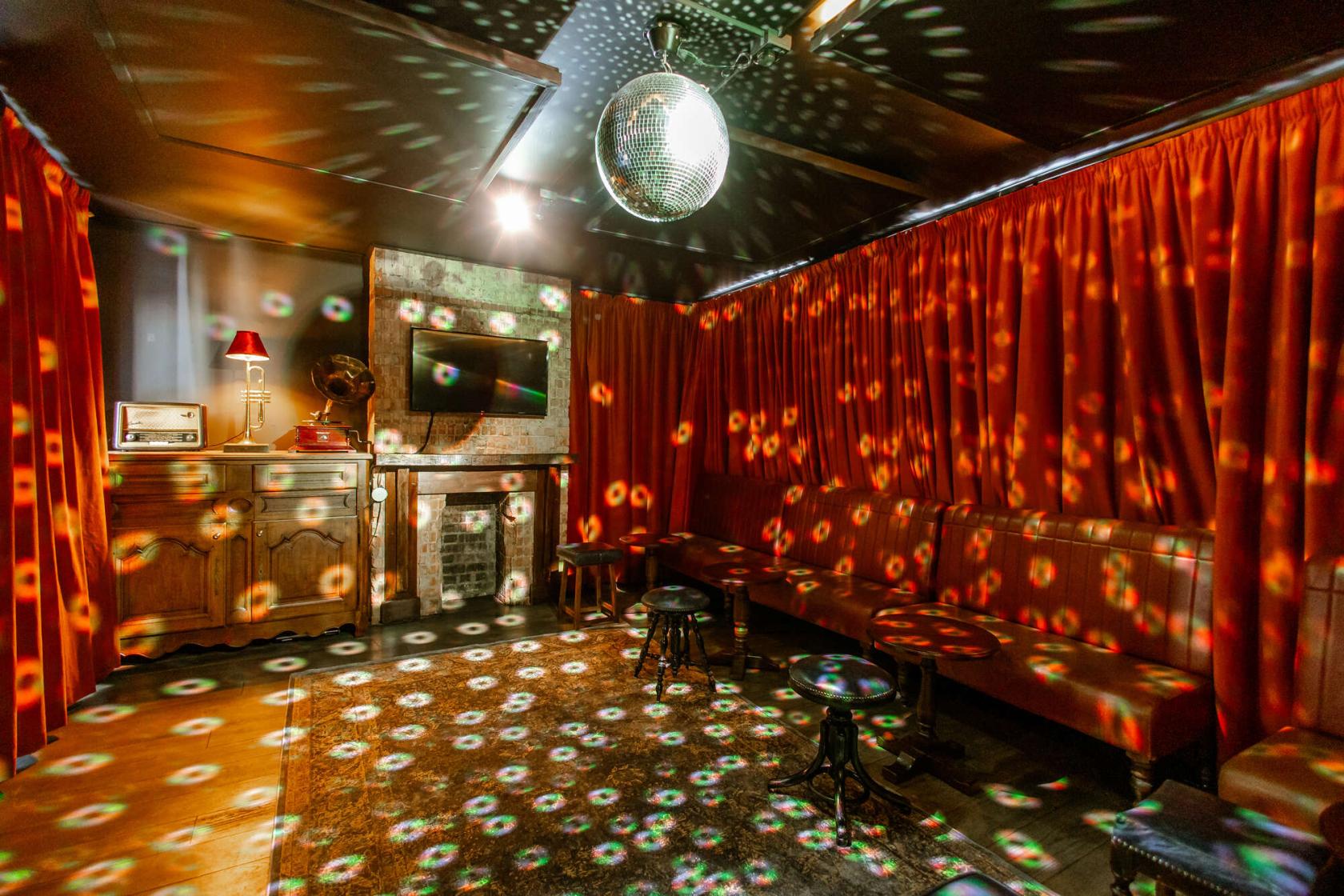 A karaoke room with a disco ball, red velvet curtains, vintage decor, and leather seating at Bow Street Tavern.