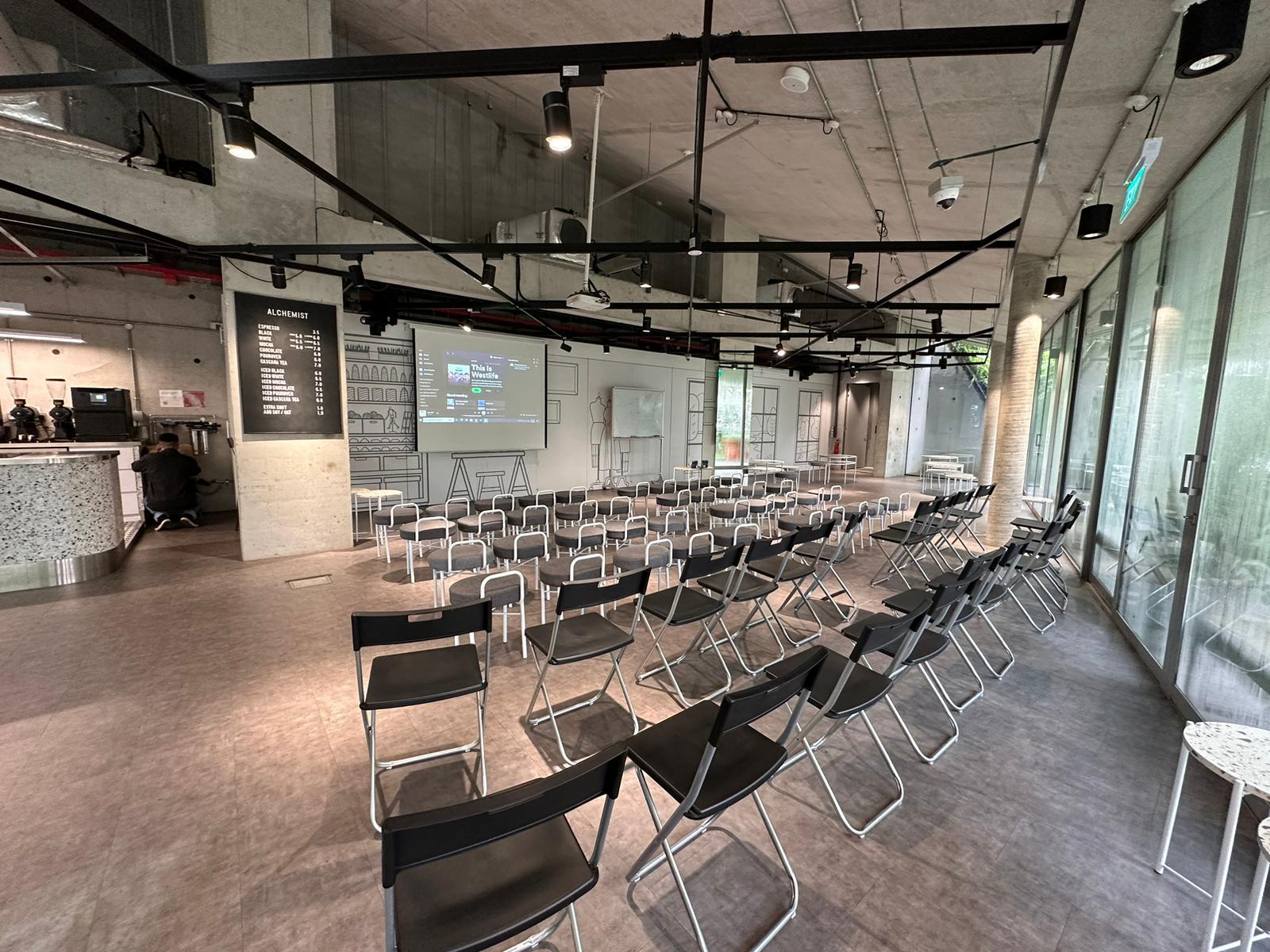 An event space with folding chairs arranged in rows, a projector screen, and floor-to-ceiling windows at The Cocoon Space.