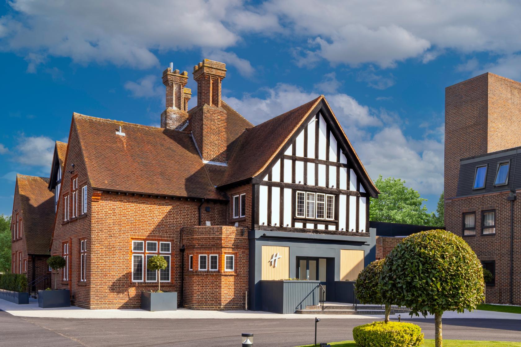 A hotel with Tudor-style timber framing, red brick exterior, and manicured landscaping at Holiday Inn London Bexley.