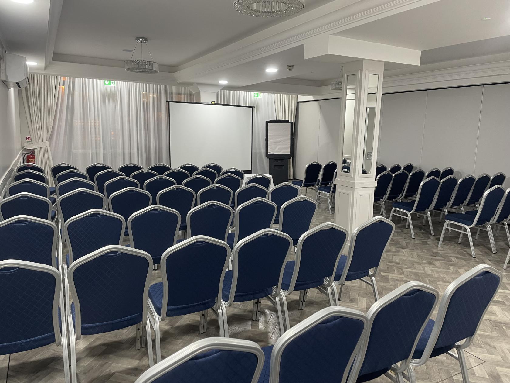An event space with rows of blue chairs facing a projector screen and flip chart at Red Lion Hotel.