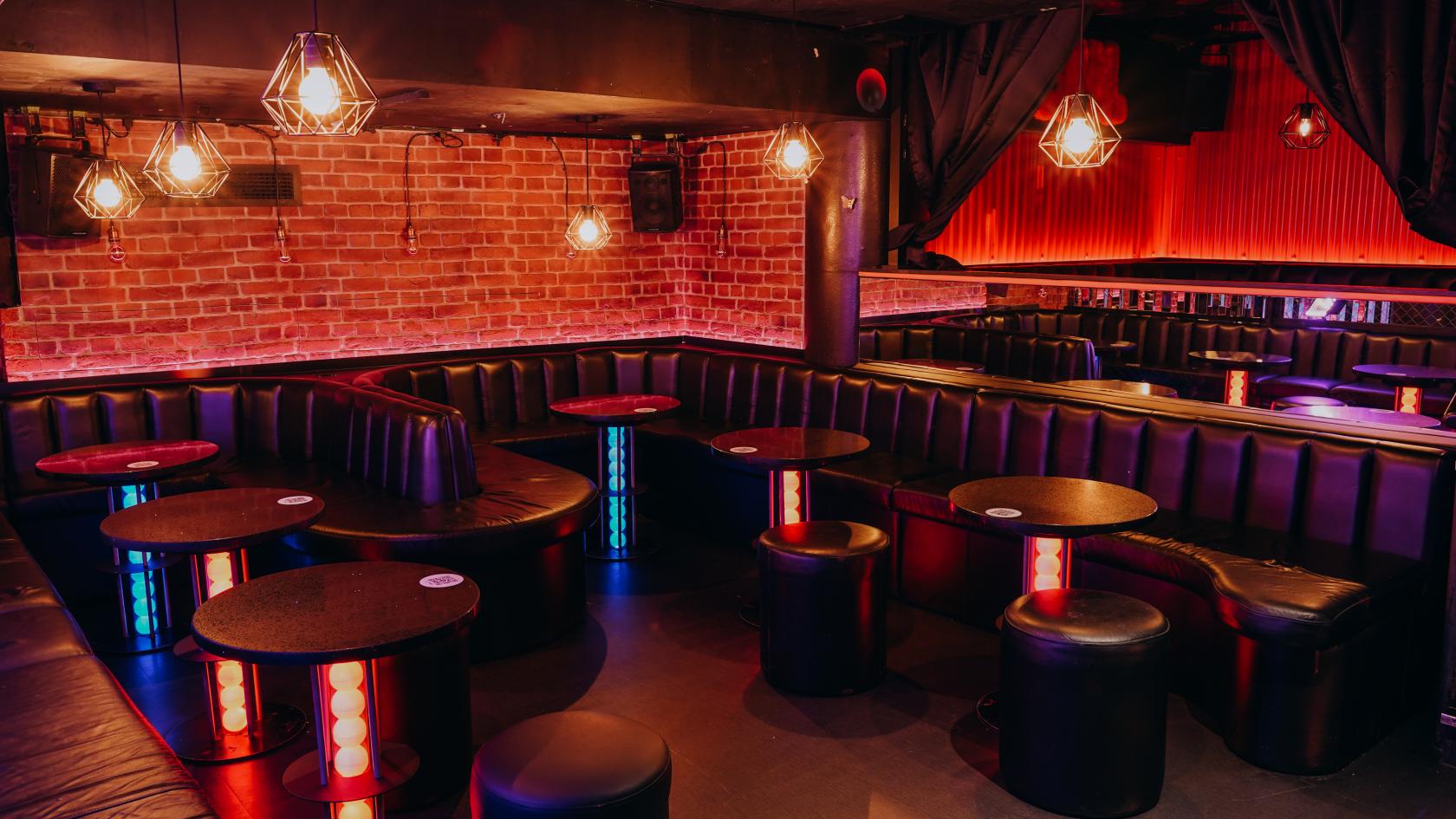 A cocktail bar with exposed brick walls, curved black leather booths, and glowing accent lighting at Ballie Ballerson London.