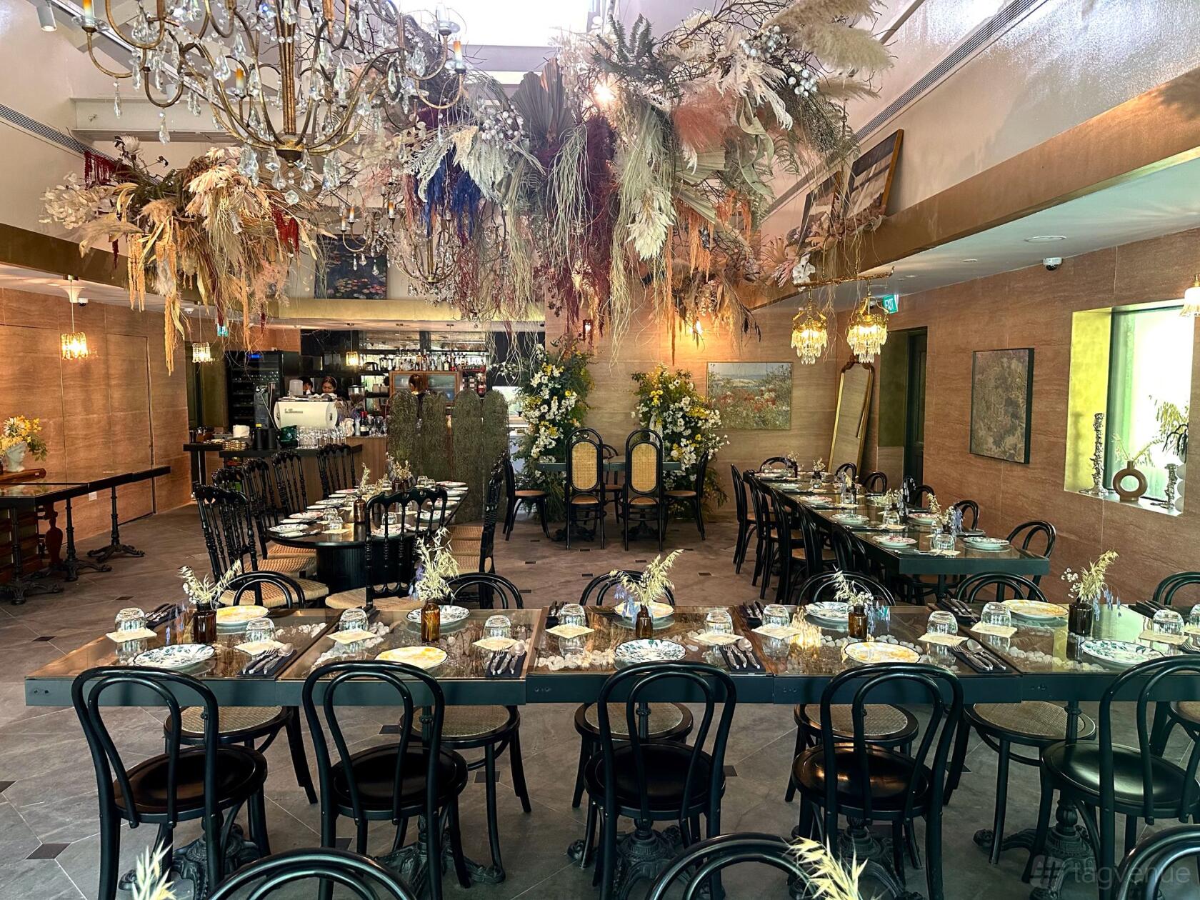 A restaurant with long dining tables, black chairs, and hanging dried floral arrangements at Le Jardin.