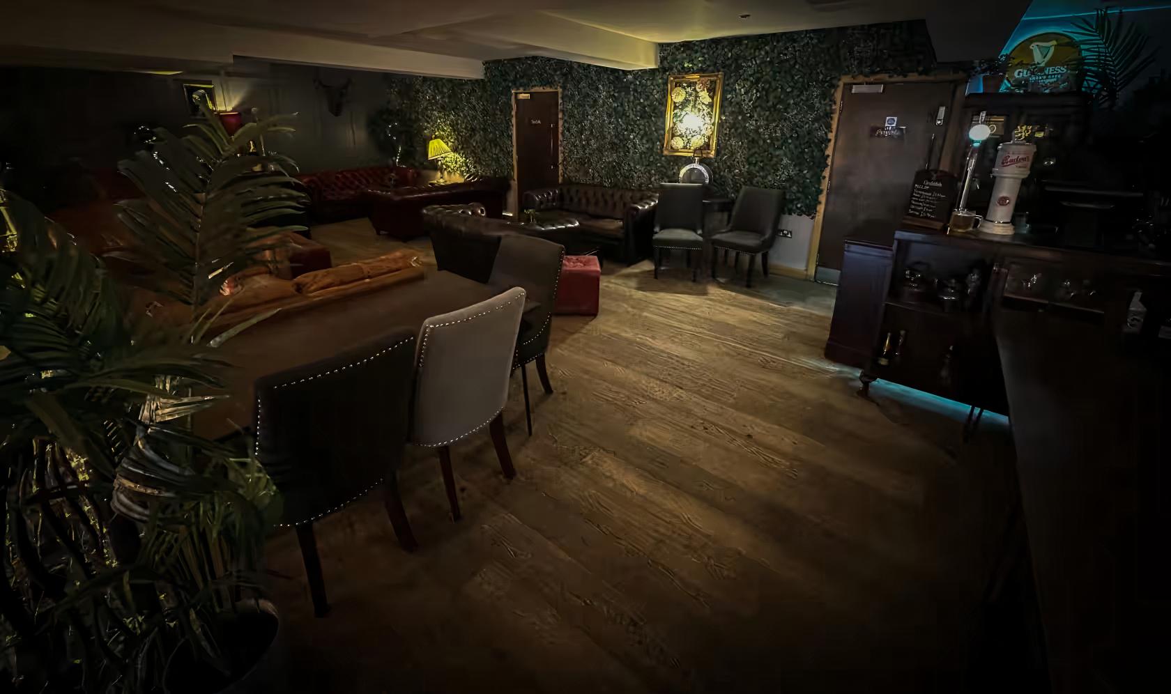 An event space in a bar with leather sofas, velvet armchairs, leafy wallpaper, and wooden floors at Lazy Lounge.