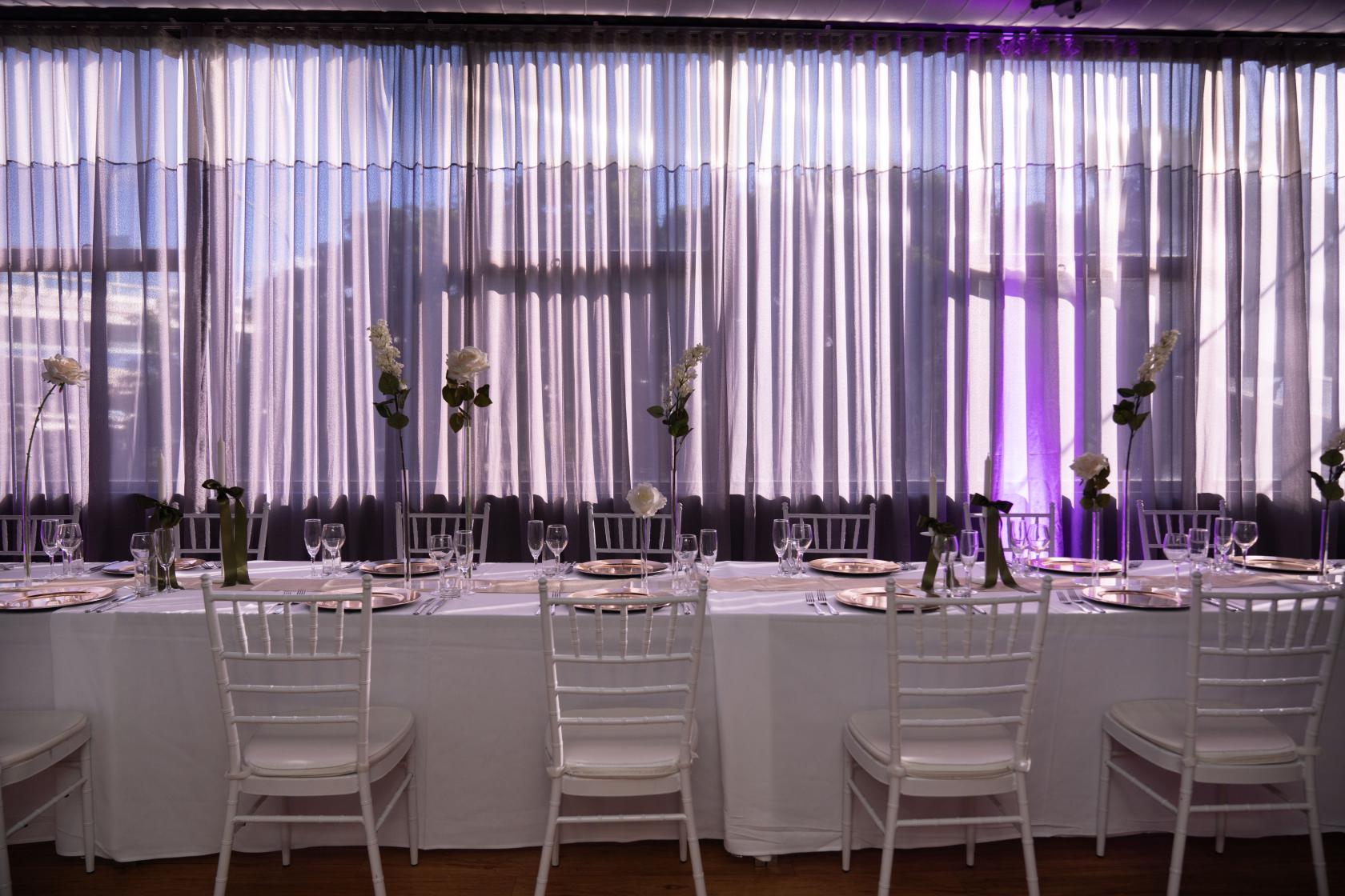 An event space with sheer floor-to-ceiling curtains, banquet table set with white linens and elegant glassware at Voco Hotel Brisbane City Centre.