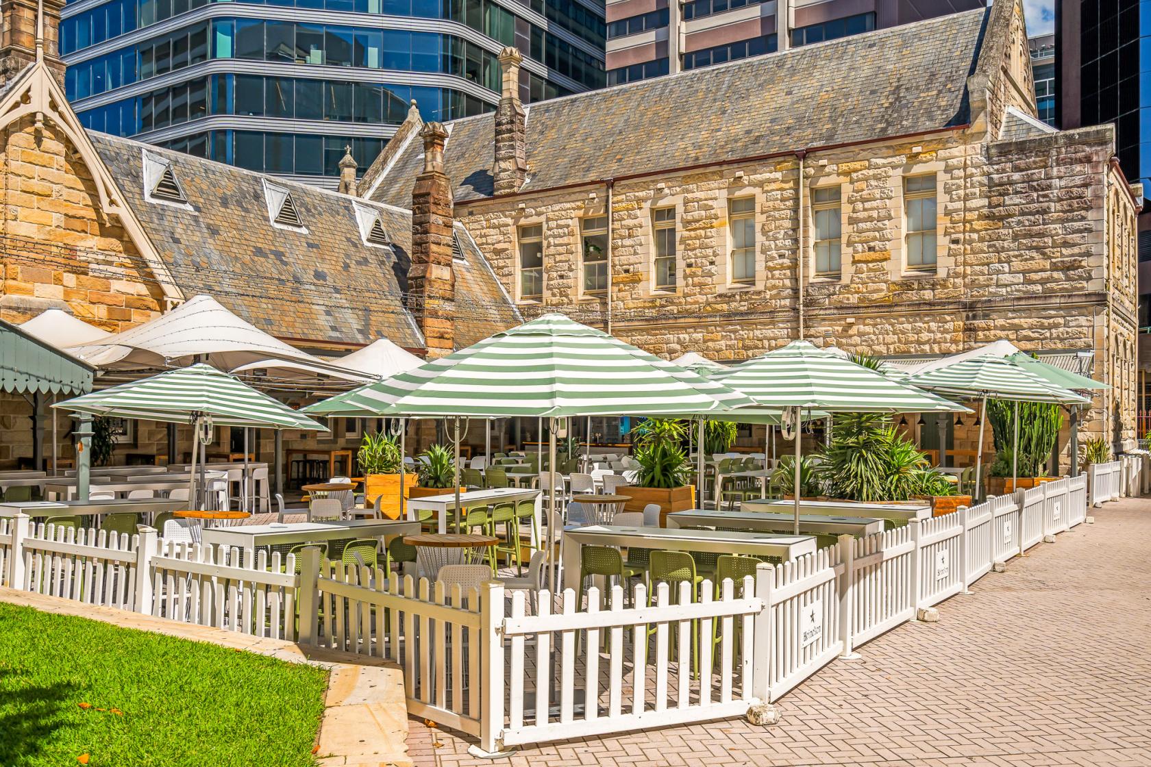 A hotel terrace with striped umbrellas, white picket fencing, and outdoor seating at Greenwood Hotel.