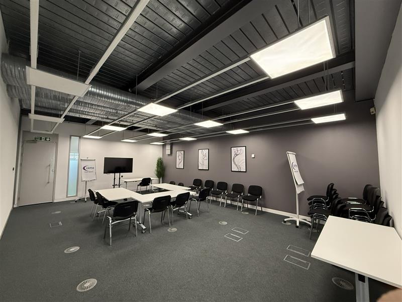 A meeting room with U-shaped tables, black chairs, wall art, and exposed ceiling panels at Event Space CEME.
