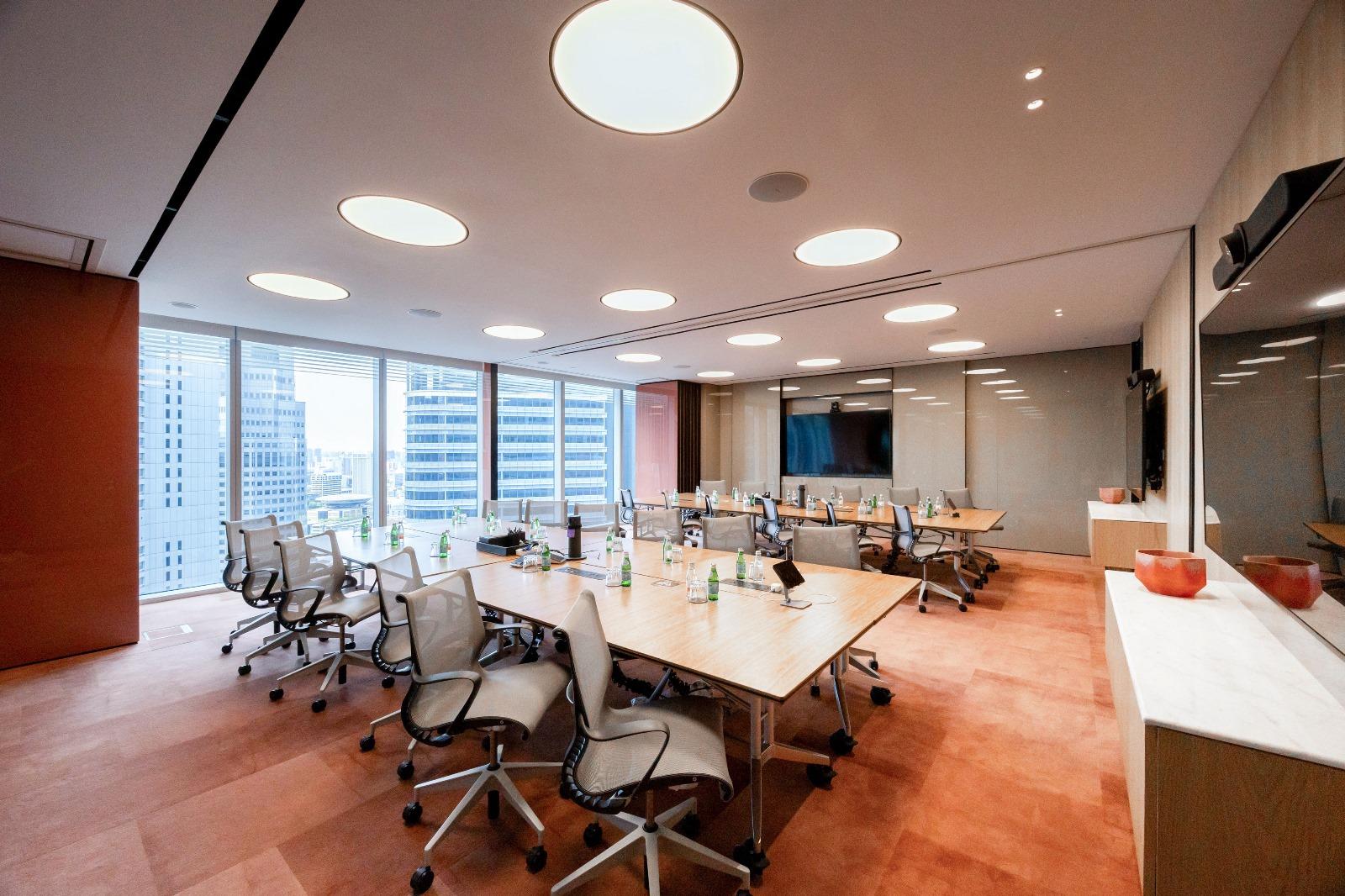A meeting room with large windows, glass walls, modular tables, ergonomic chairs, and bottled water at Ocean Financial Centre.
