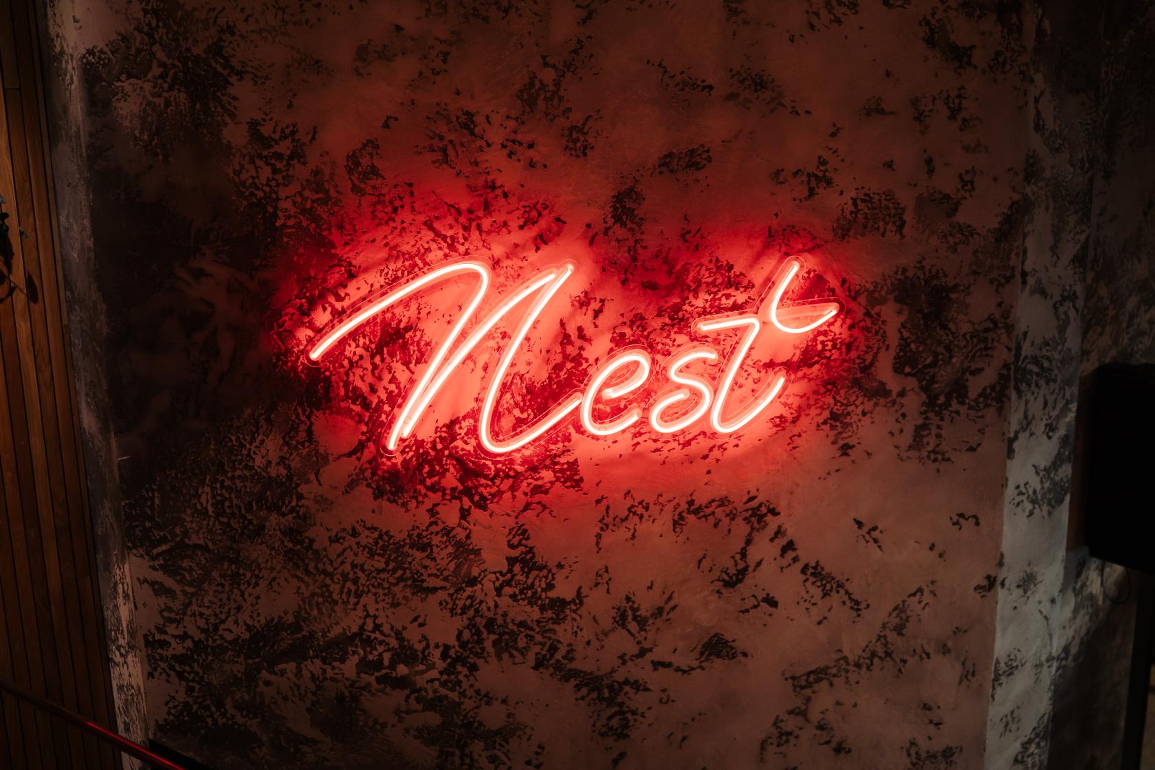 An exposed concrete wall with a glowing red neon 'Nest' sign at NEST BISHOPSGATE.