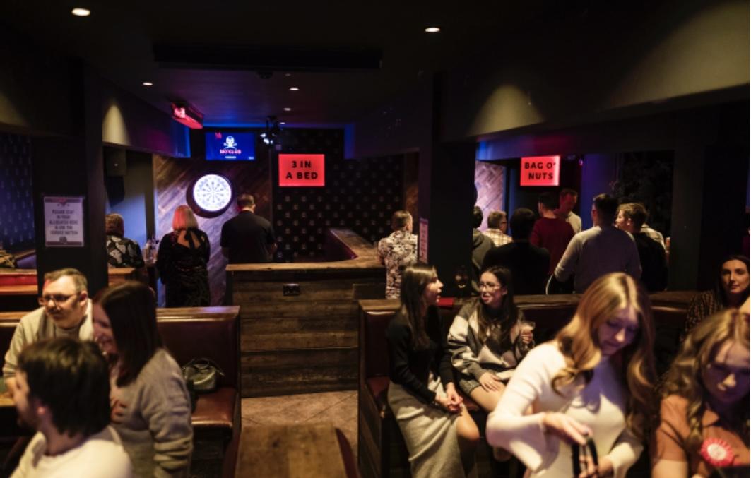 A barn-style pub with dartboards, wooden seating booths, and neon signs at The Rectory - 180 Club.
