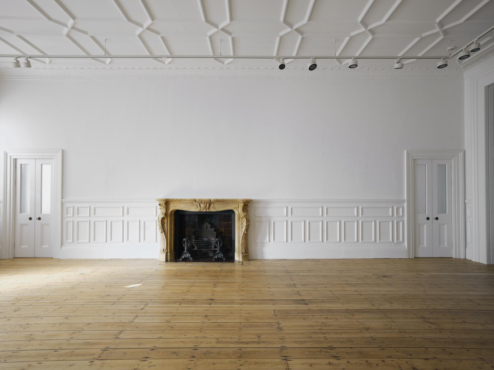 An event space in a restaurant with a decorative fireplace, white paneled walls, and hardwood floors at The Lavery.