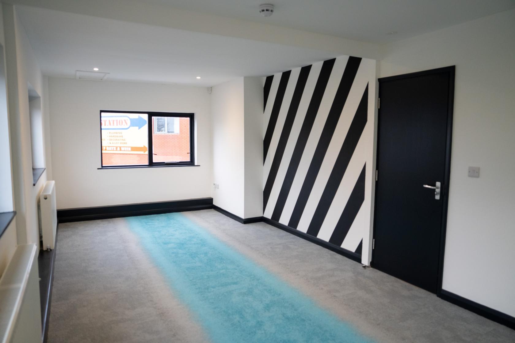 A function room with a striped accent wall, blue carpet runner, and large window at Eloquent Arts Centre.