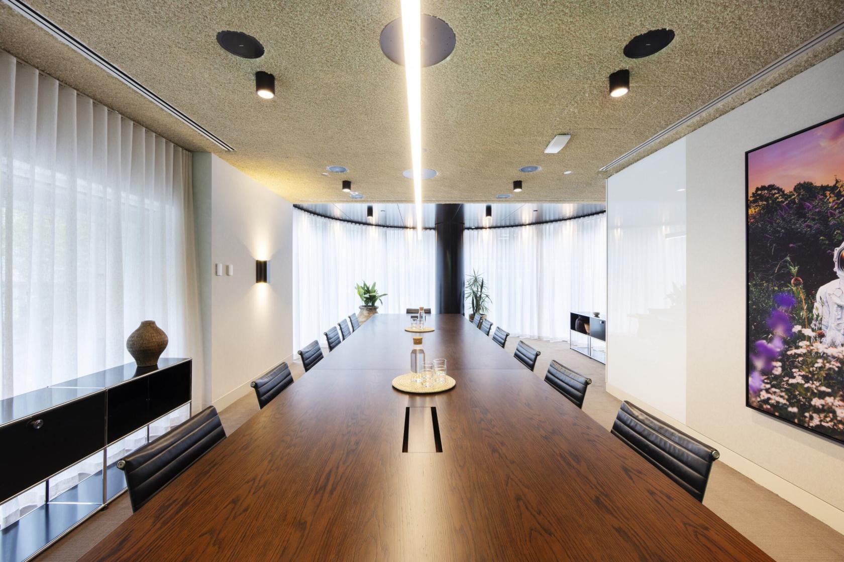 A meeting room with a long wooden boardroom table, black leather chairs, natural light, and sheer curtains at Space&Co. 530 Collins Street.