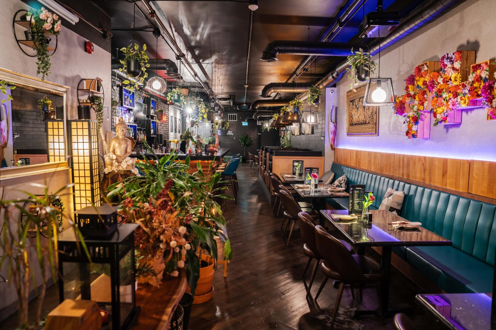 A restaurant with teal banquette seating, wooden tables, hanging plants, and colorful wall art at Crystal Thani Kitchen And Bar.