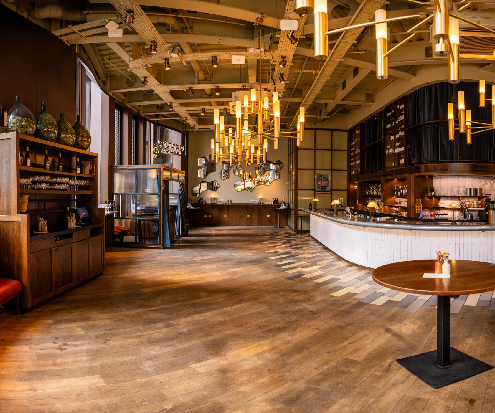 A restaurant with wooden floors, pendant lighting, mirrored wall decor, and a curved bar at Vinoteca City.