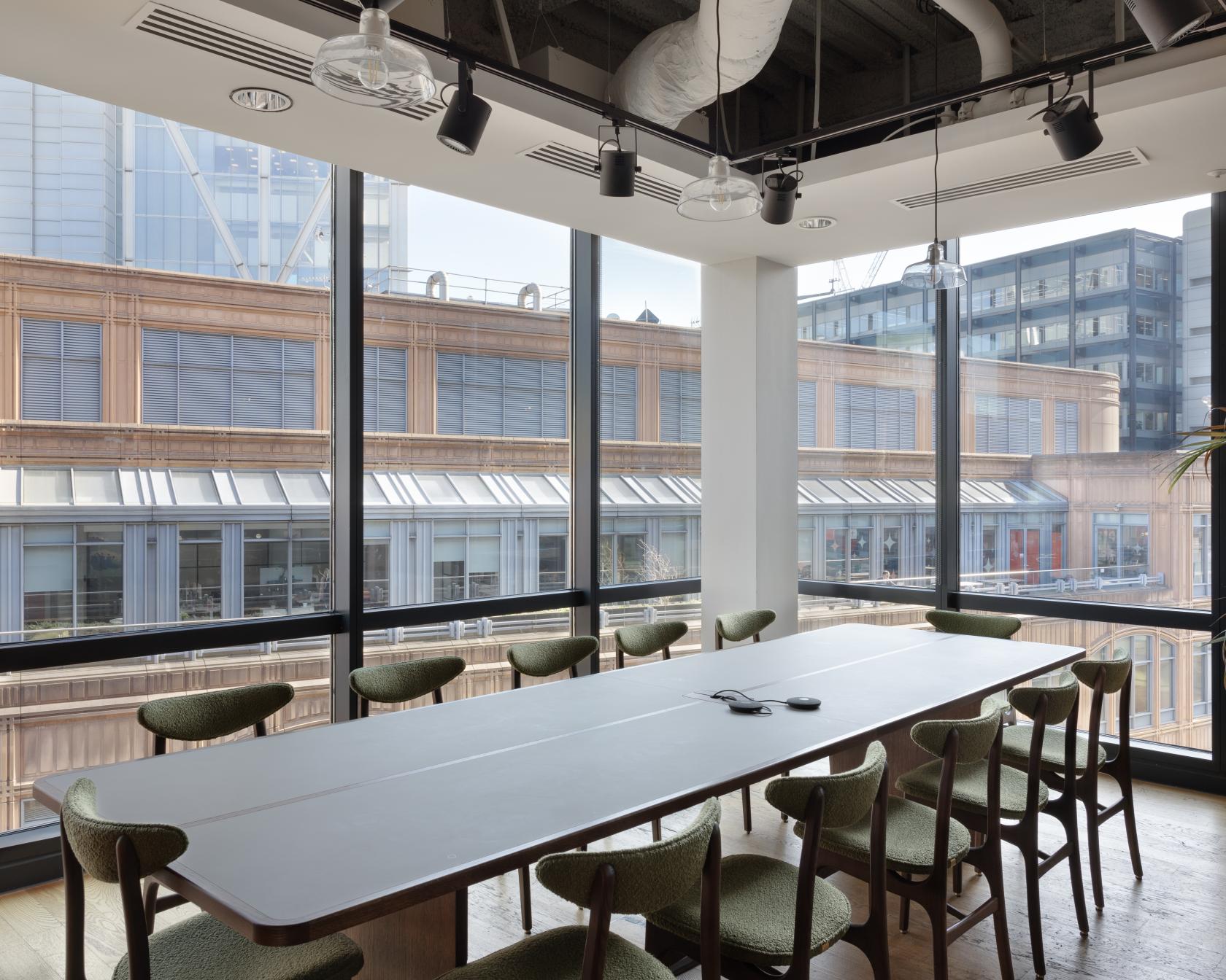 A meeting room with floor-to-ceiling windows, a long conference table, and modern green chairs at Mindspace Shoreditch.