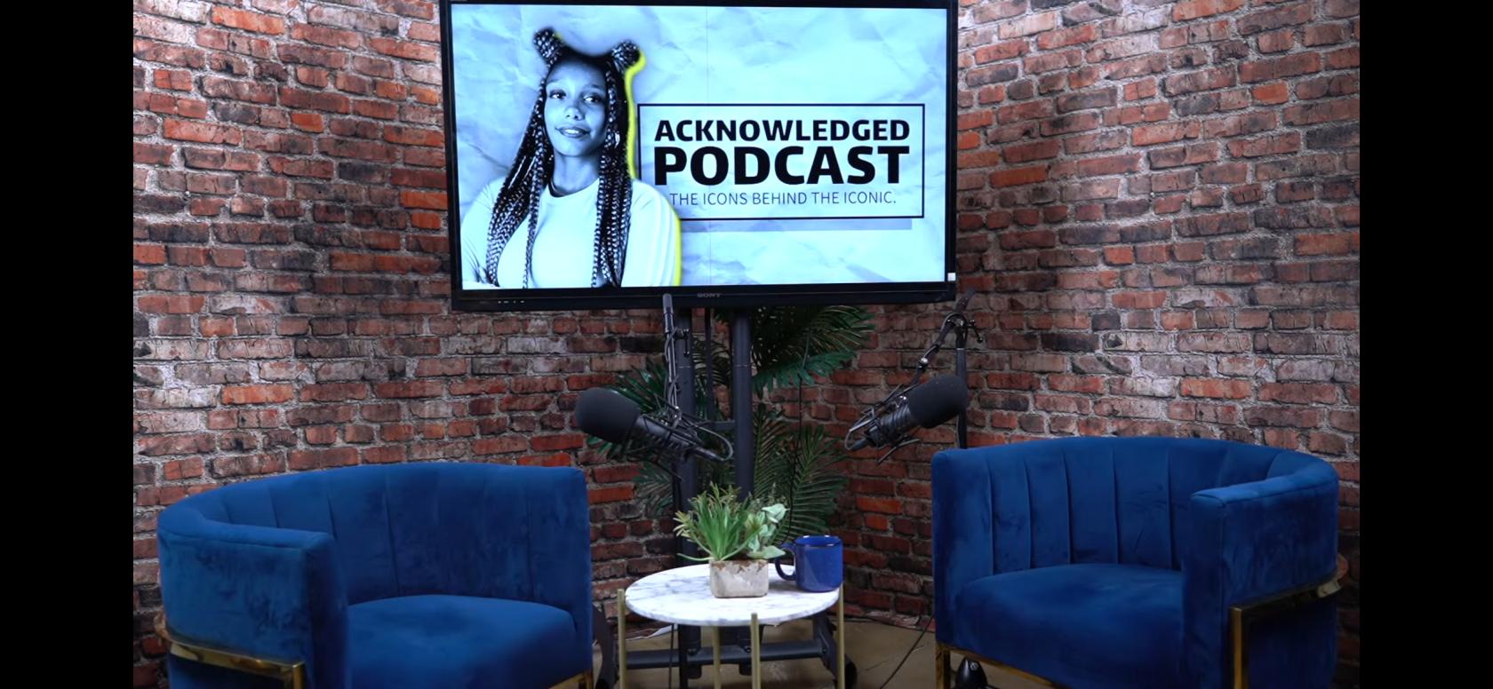 A podcast studio with exposed brick walls, blue velvet chairs, and a mounted screen at Podstream Studios.