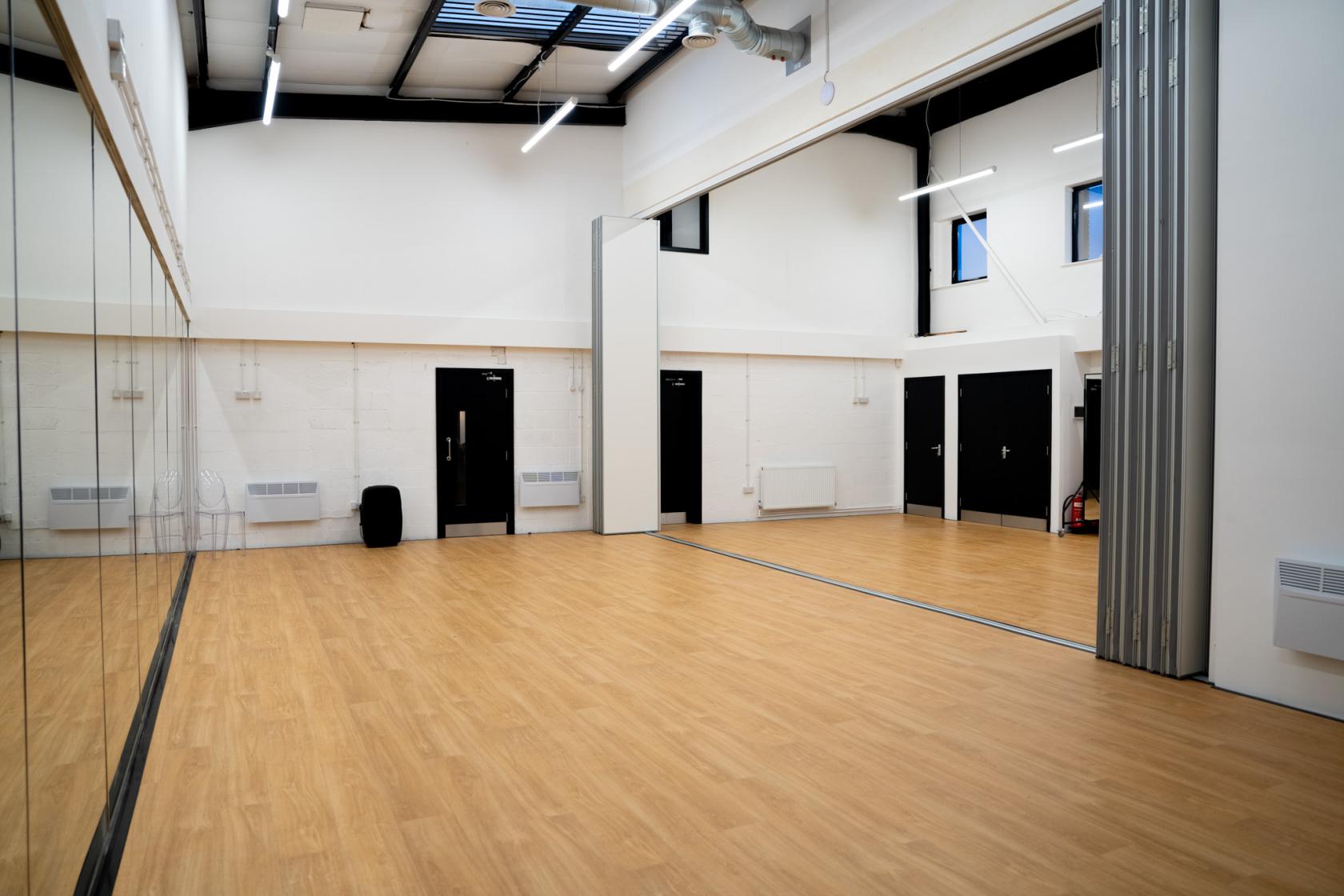 An event space with high ceilings, wood flooring, mirrored wall, and partition at Eloquent Arts Centre.