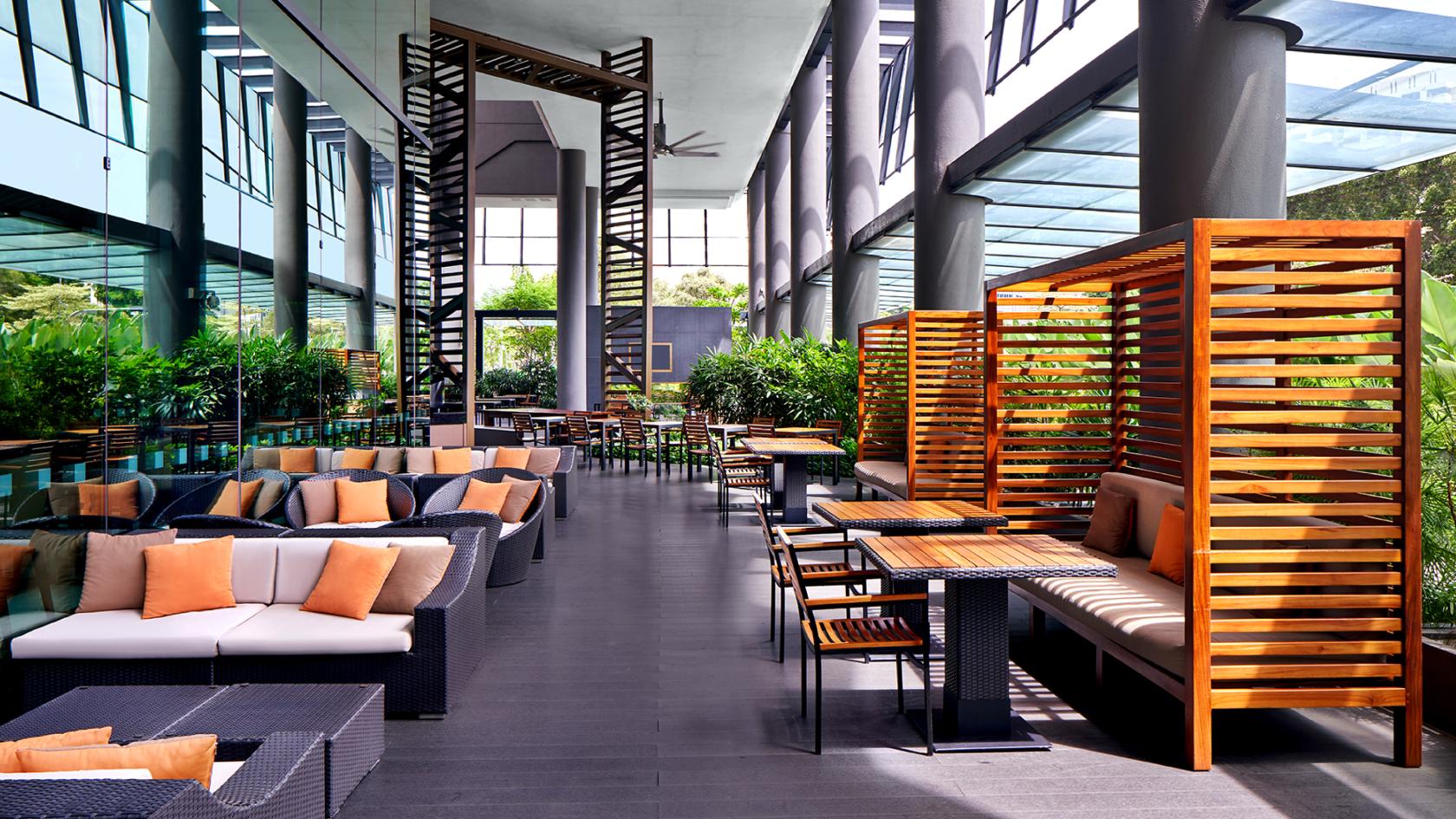 An outdoor space with woven sofas, wooden cabanas, and greenery at Holiday Inn Express Singapore Clarke Quay.