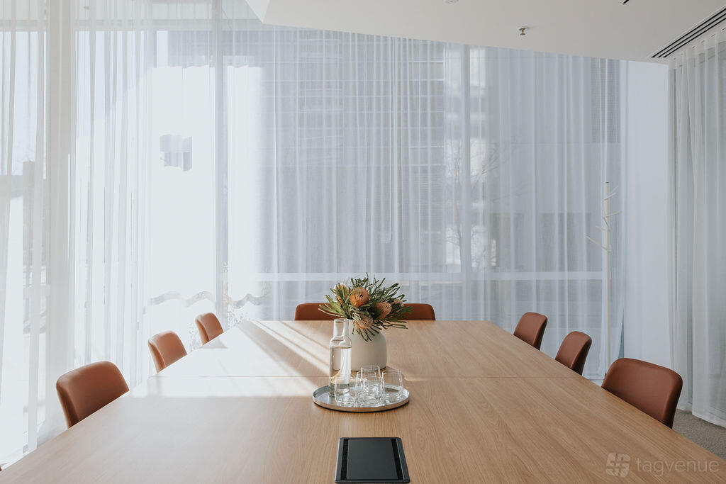 A meeting room with a large wooden table, brown chairs, sheer curtains, and a floral centerpiece at Flex by ISPT Pathway Place.