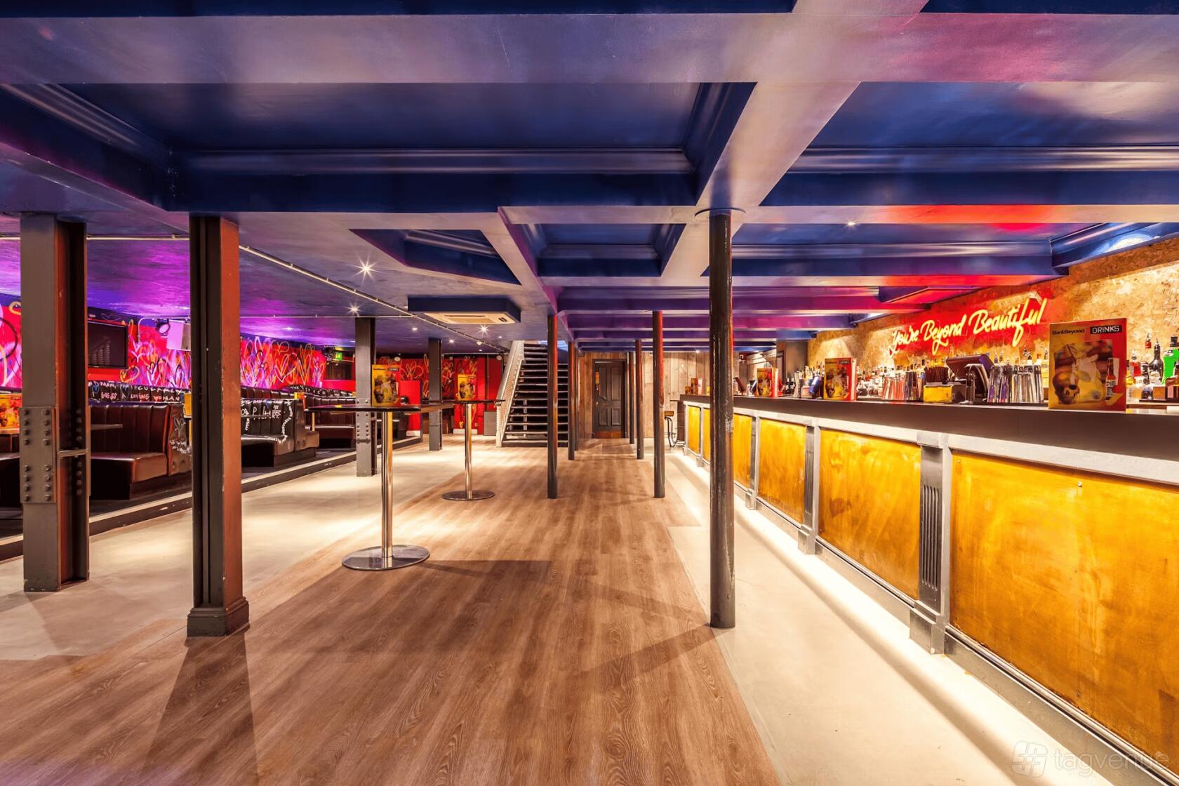 An event space in a bar with wooden floors, exposed ceiling beams, and a long illuminated bar at Bar & Beyond Norwich.