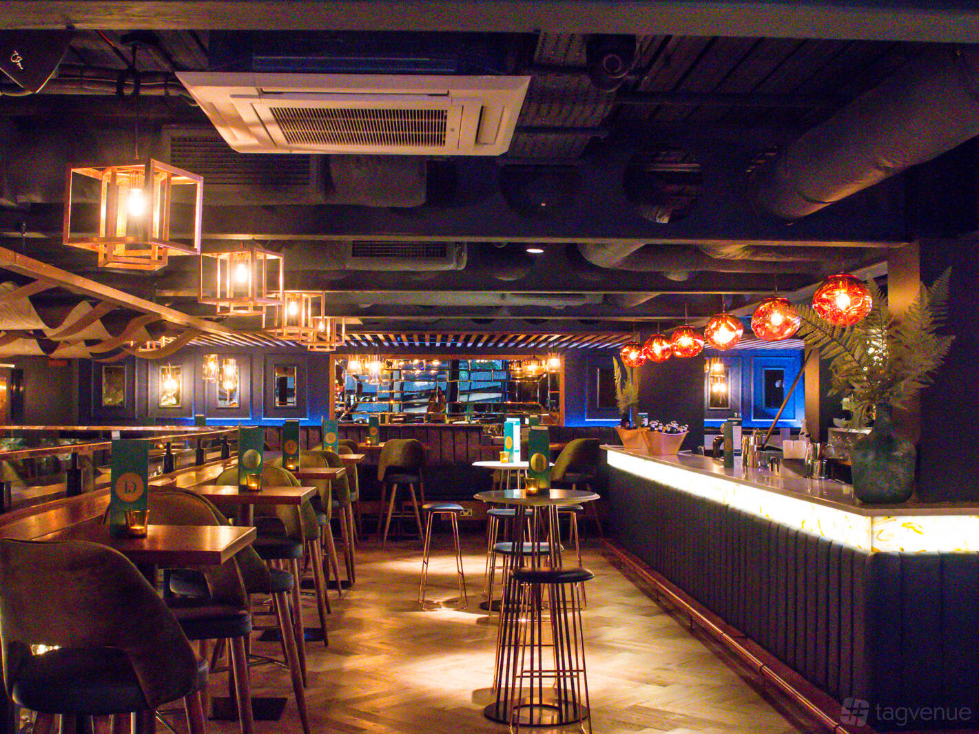 An event space with a long bar, high tables, pendant lighting, and plush seating at Banyan Spinningfields.