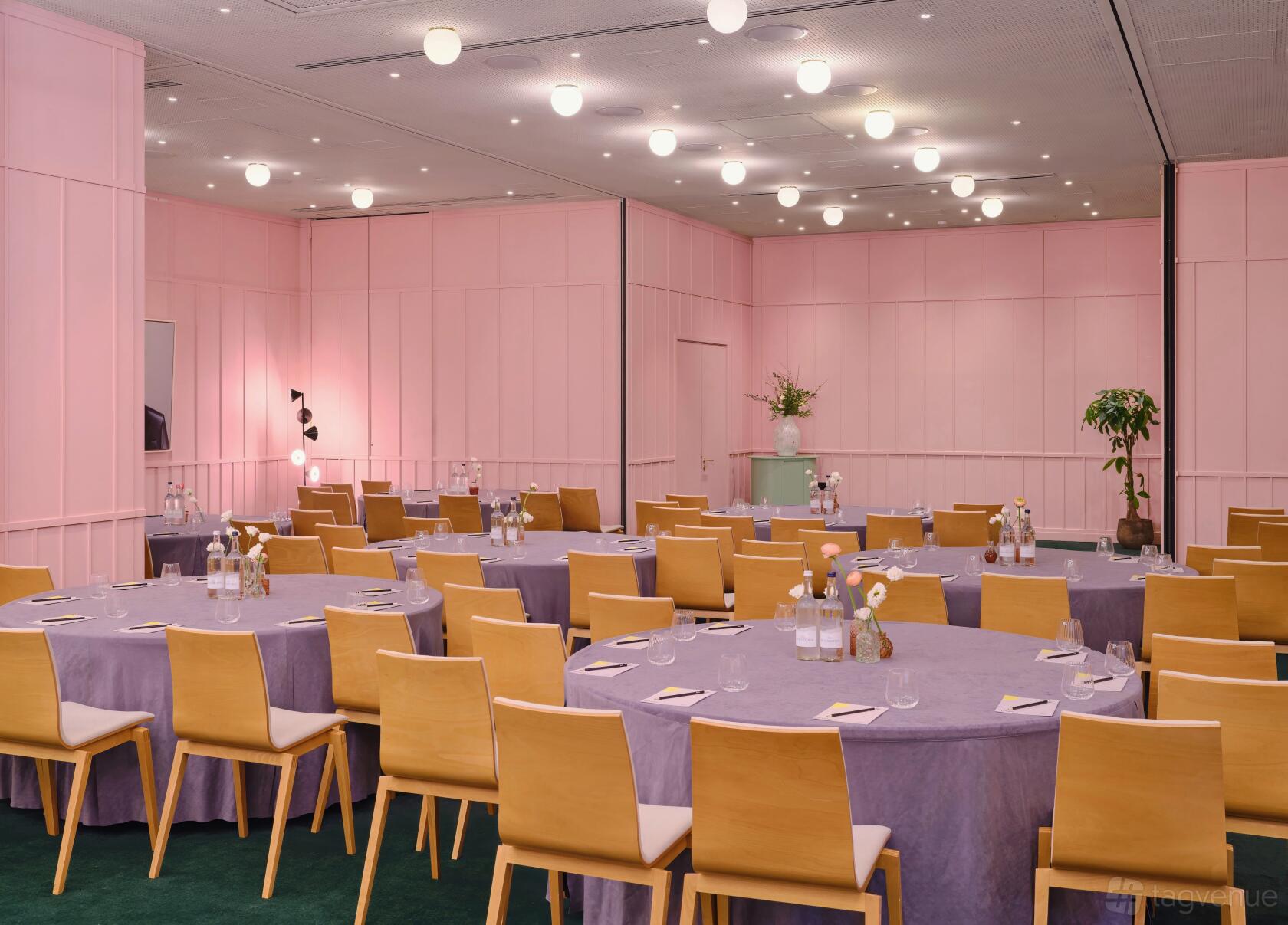 An event space with pastel pink walls, round tables draped in lilac linens, and light wood chairs at art'otel London Battersea Power Station.