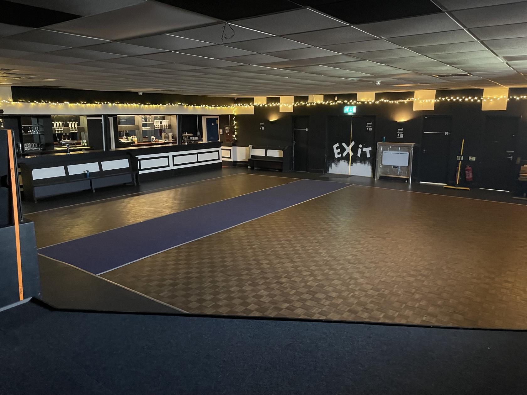 An event venue with a large open dance floor, string lights, and a bar area at Arena Music Venue.