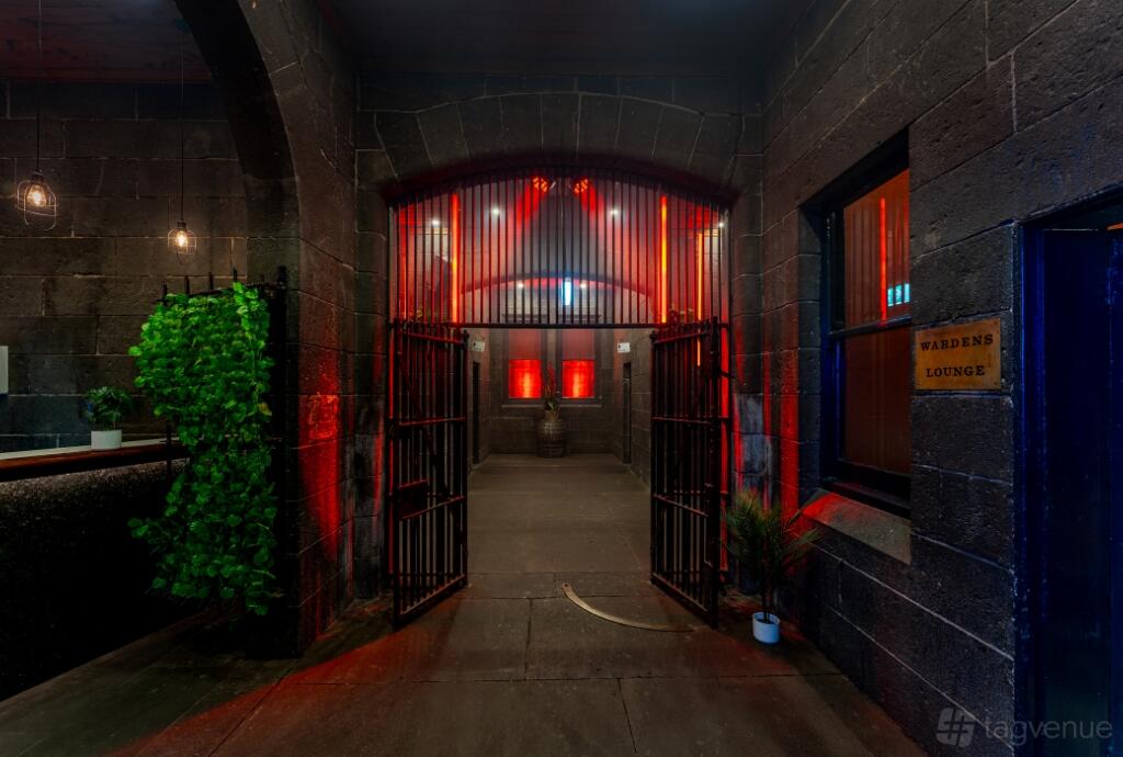 An event space with exposed stone walls, red uplighting, and iron-barred gates at Royal Melbourne Hotel.