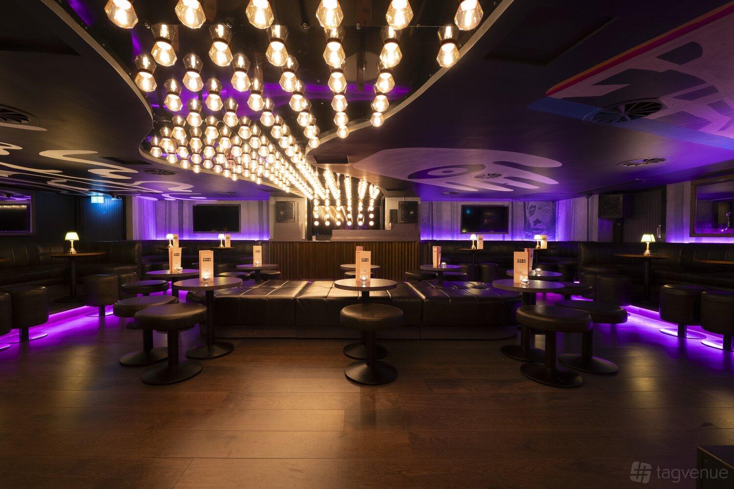 An event space in a bar with purple underlighting, rows of pendant bulbs, and dark leather seating at Coco.