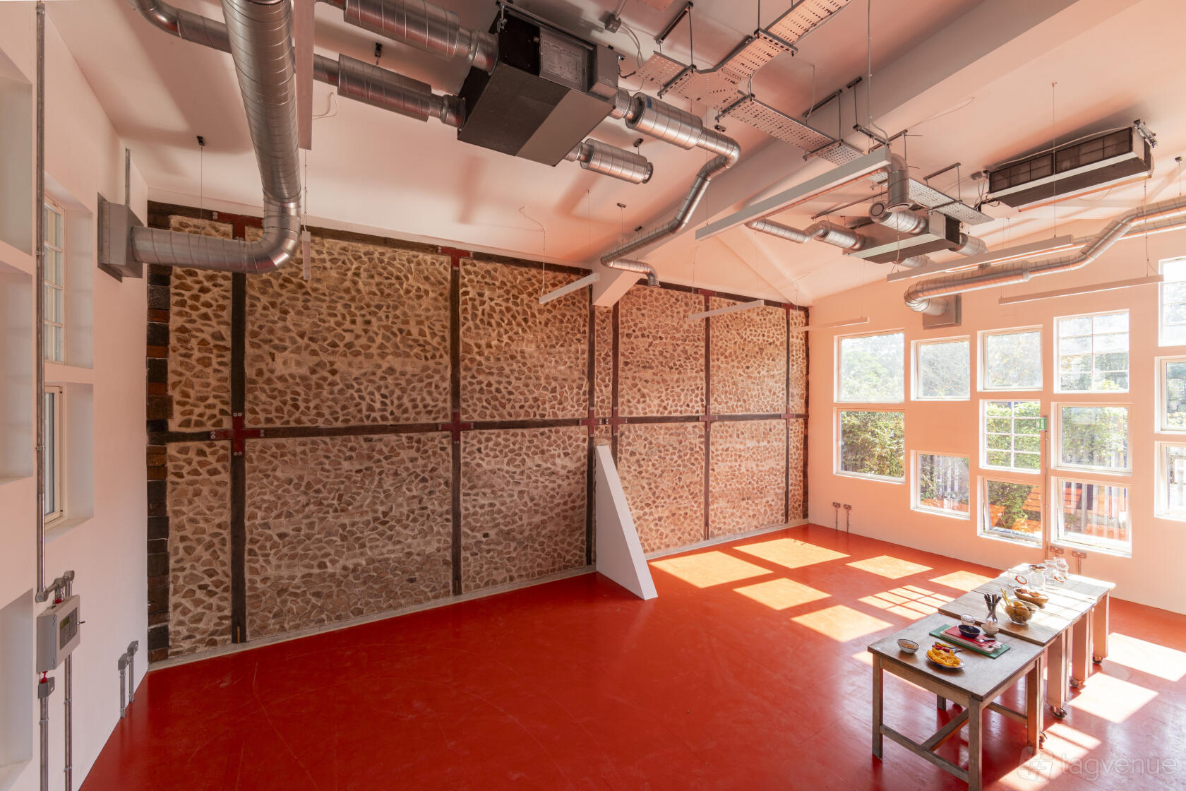 A classroom with exposed stone walls, red flooring, large windows, and a table set with refreshments at Paper Garden.