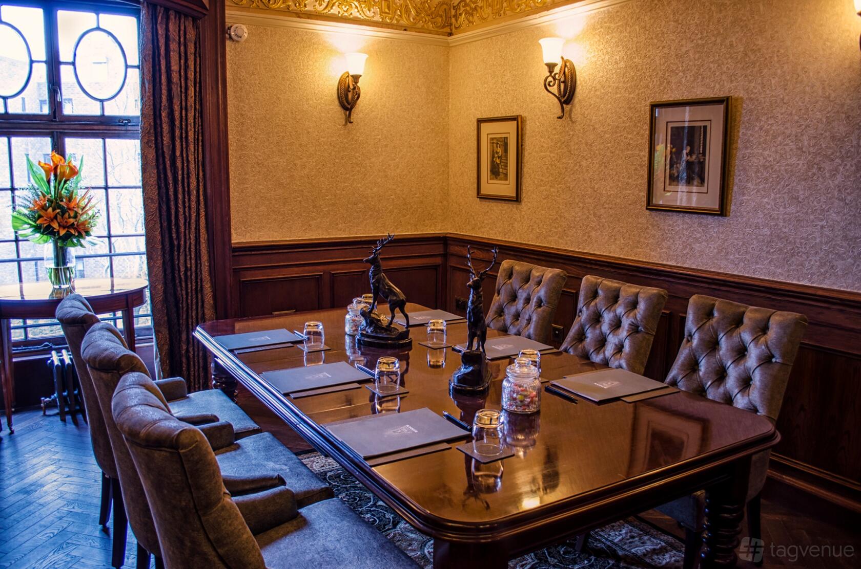A hotel function room with a polished wood table, tufted chairs, wall sconces, and framed artwork at The Bonham Hotel.