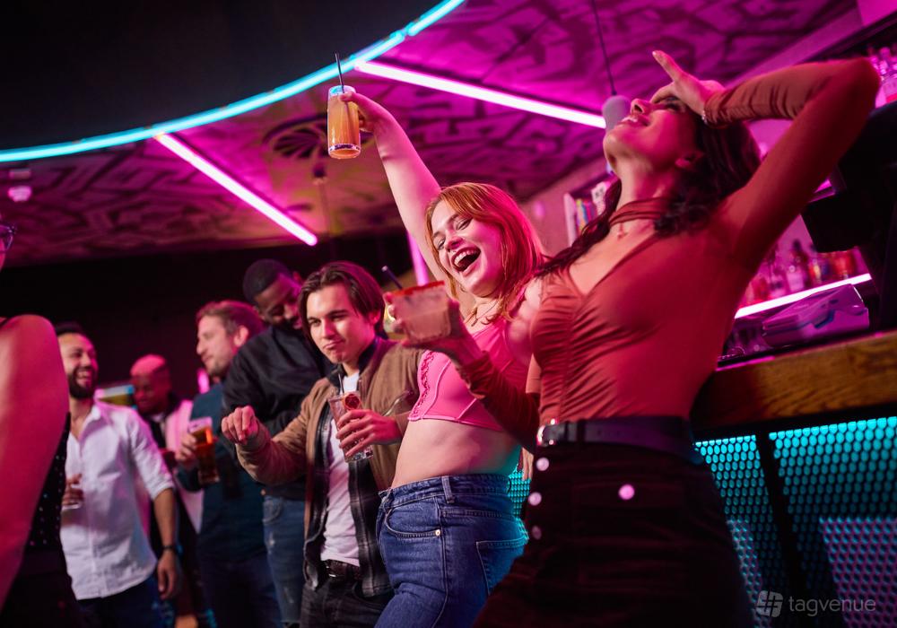A lively bar with neon lighting, people dancing and holding drinks at Boom Battle Bar Manchester.