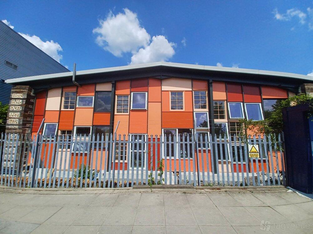 A meeting centre with a colorful geometric facade, large windows, and metal fencing at Paper Garden.