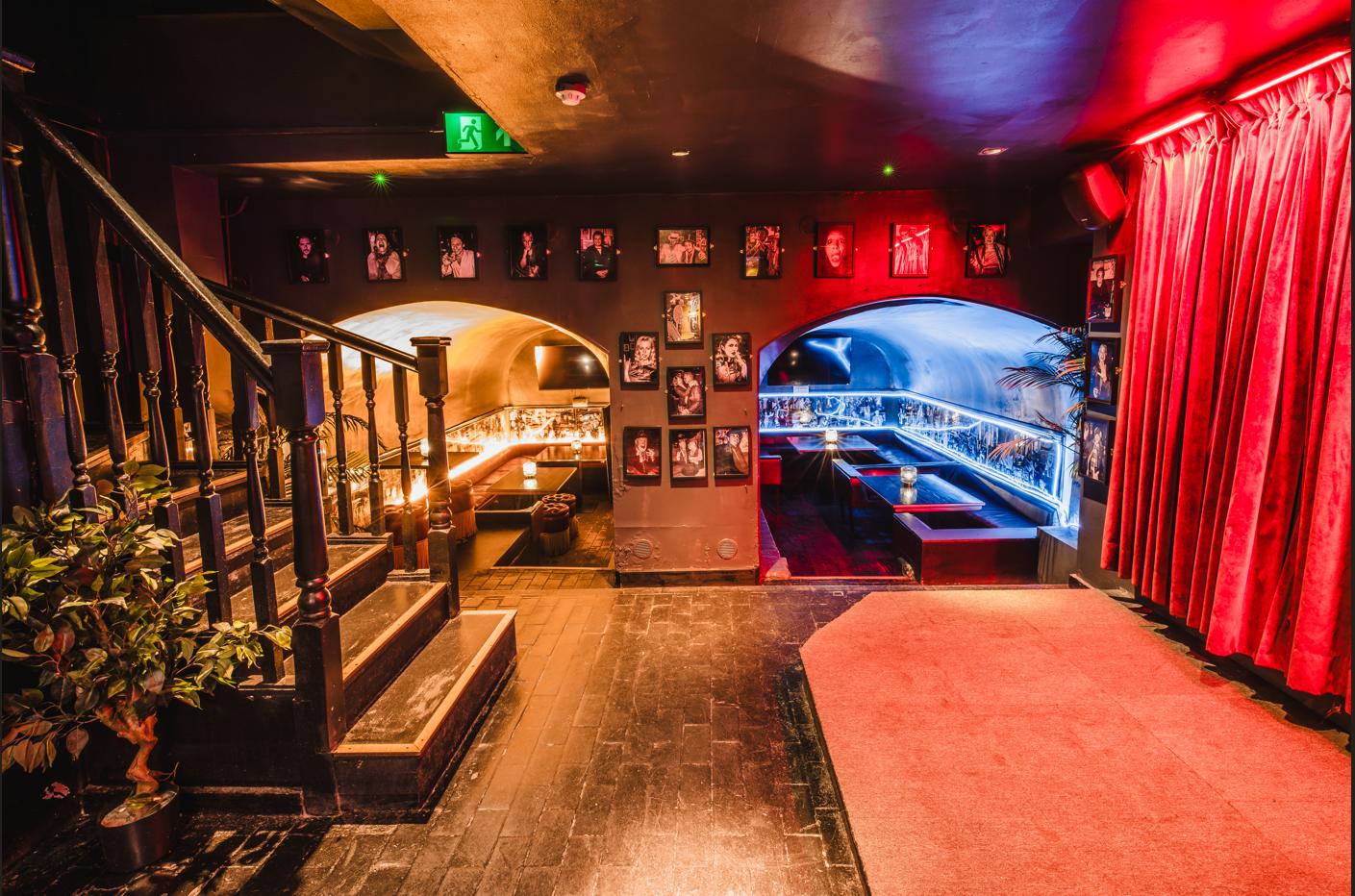 An event space in a bar with red velvet curtains, black-and-white photos on the walls, and cozy booth seating at Greek Street Live.