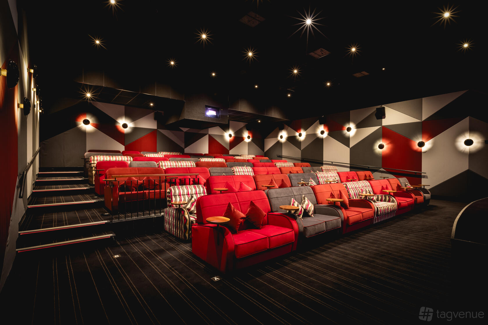An auditorium with plush red and gray sofas, geometric patterned walls, and wall-mounted lights at Everyman Stratford-Upon-Avon.