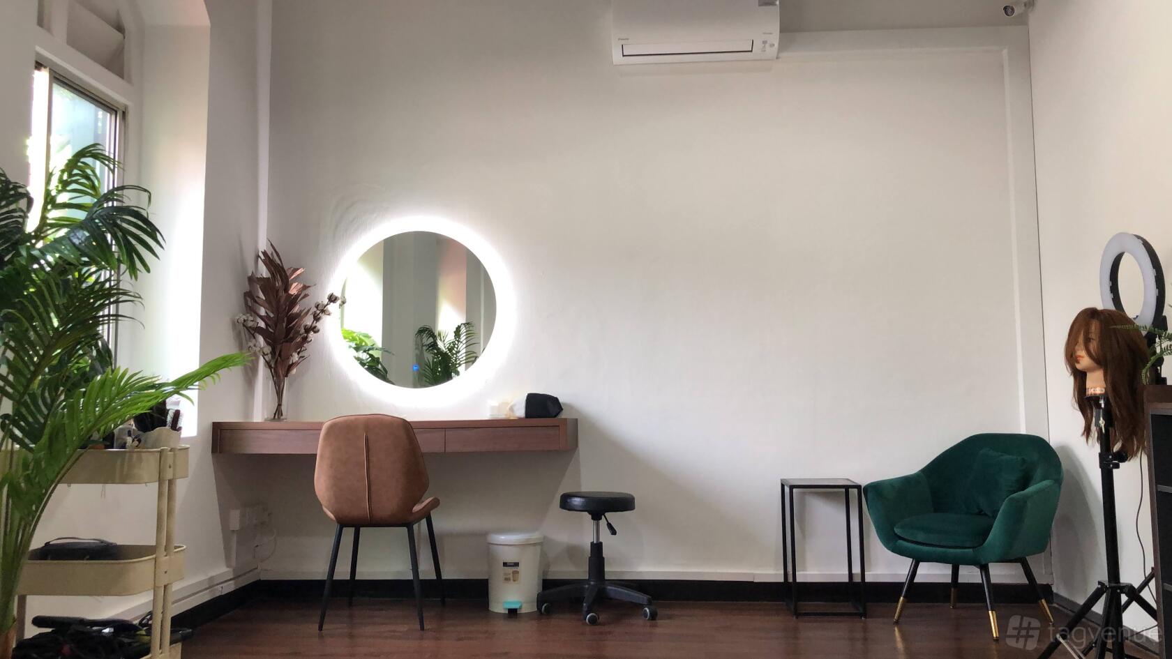 A photo studio with a round backlit makeup mirror, brown chair, green armchair, and wood floors at Makeup Maestro.