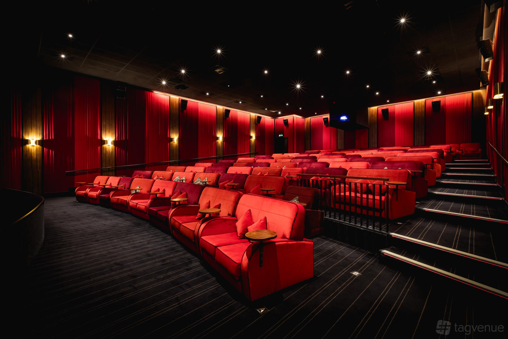 An auditorium with tiered red velvet armchairs, striped carpeting, and wall sconces at Everyman Stratford-Upon-Avon.