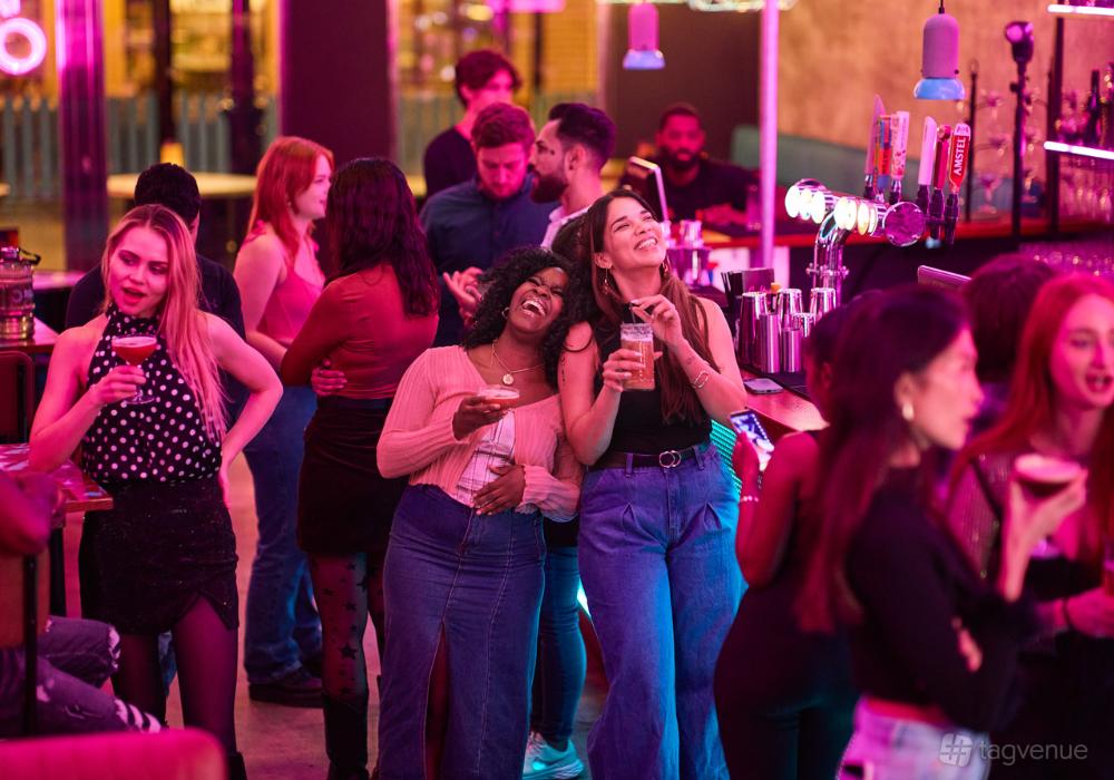 A lively bar with neon lighting, a central bar counter, and guests enjoying cocktails at Boom Battle Bar Leeds.