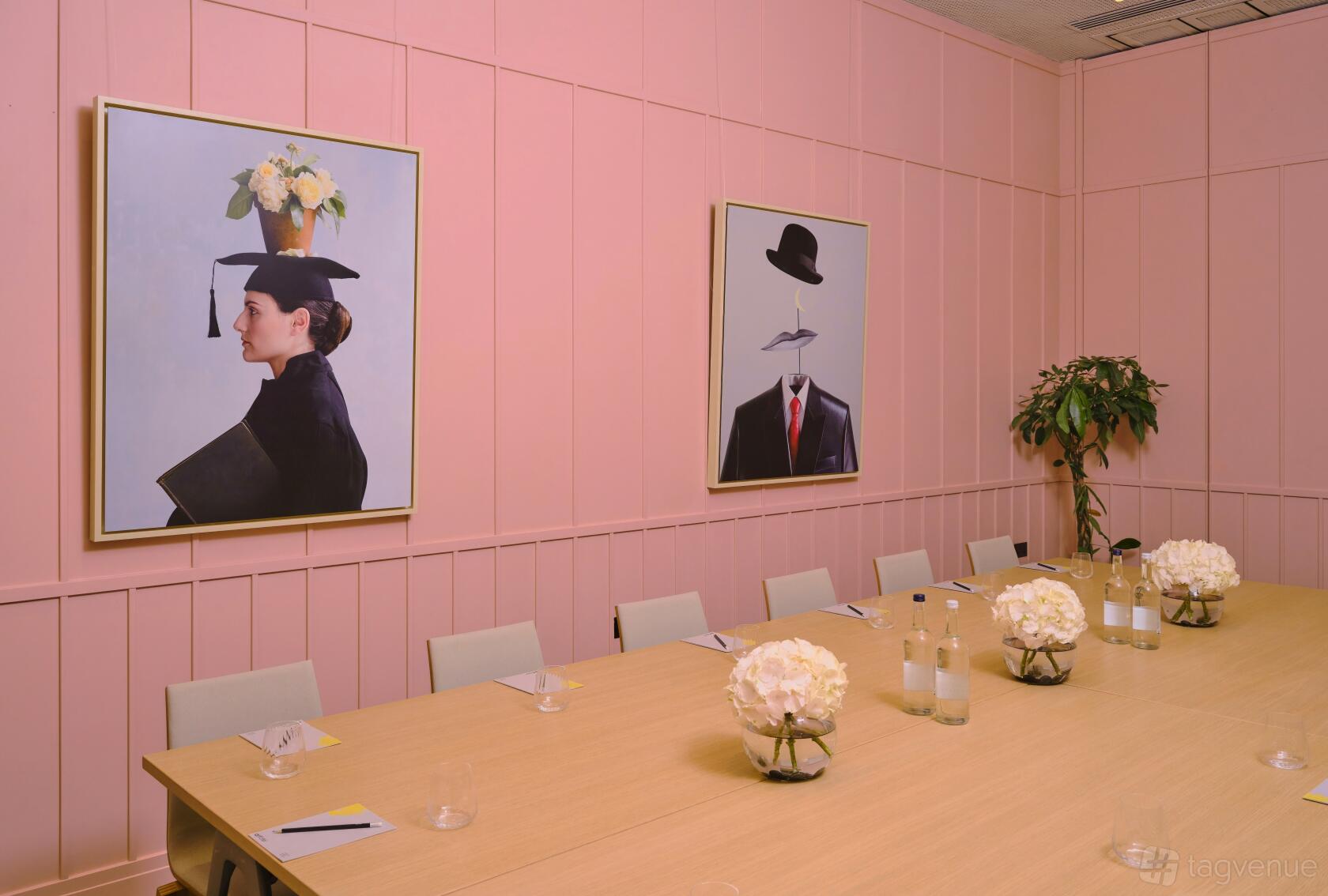 An event space with pink paneled walls, modern artwork, and a long table with white floral centerpieces at art'otel London Battersea Power Station.