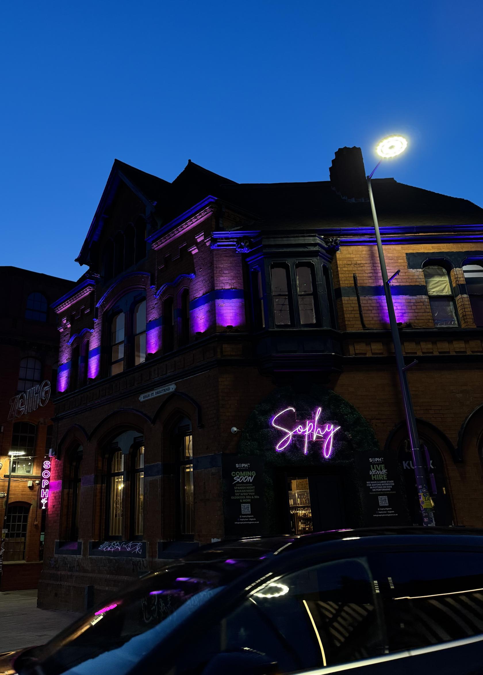 A pub with exposed brick facade and purple neon lights highlighting arched windows at Sophy.