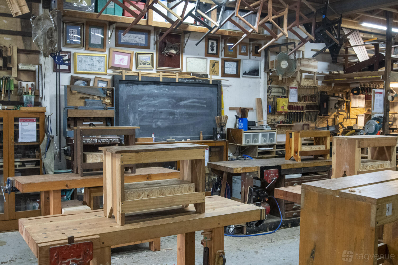 An art studio with wooden workbenches, a chalkboard, framed artwork, and woodworking tools at Among The Trees.