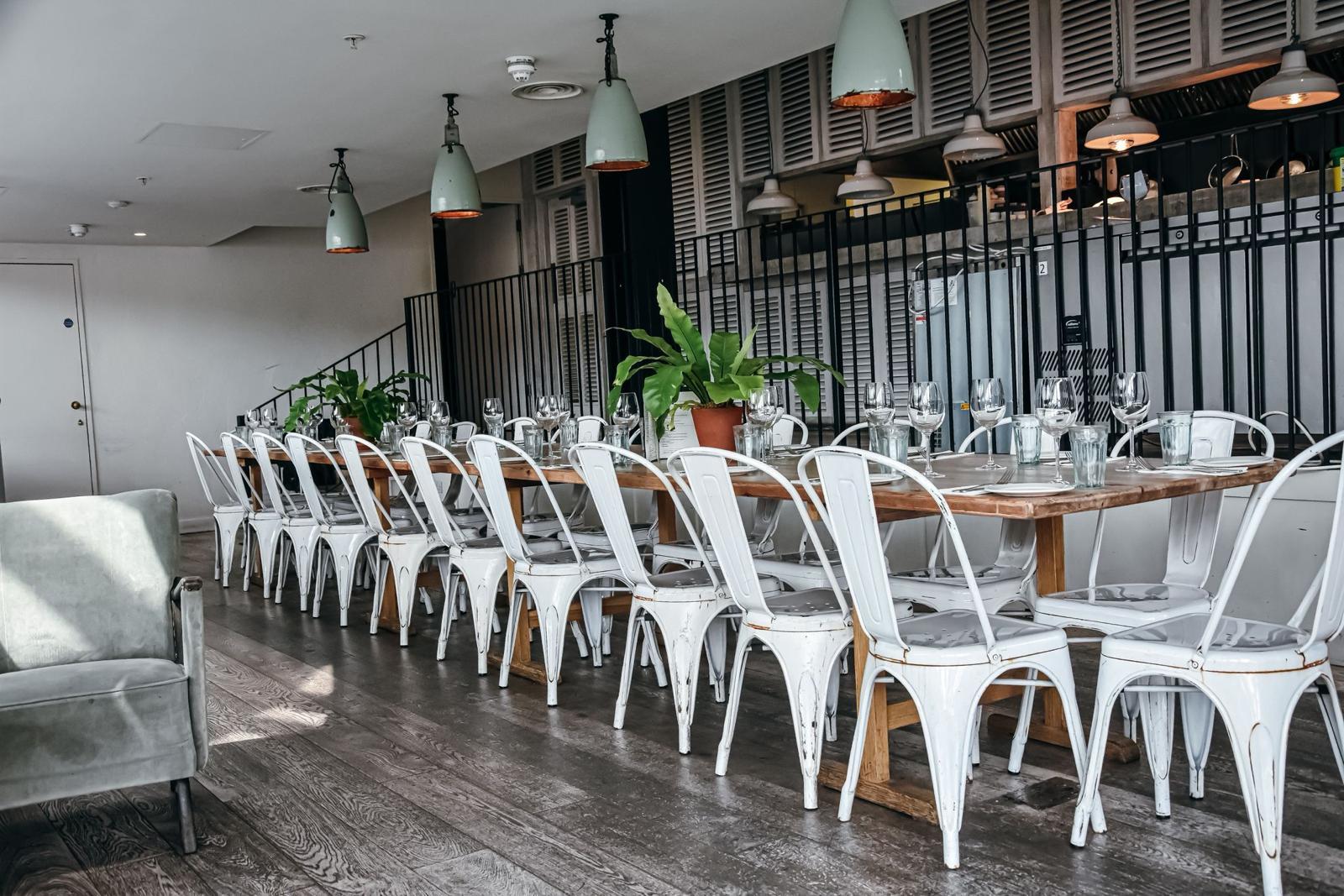 An event space with long wooden tables, white metal chairs, and potted plants at 601 Queen's Road.