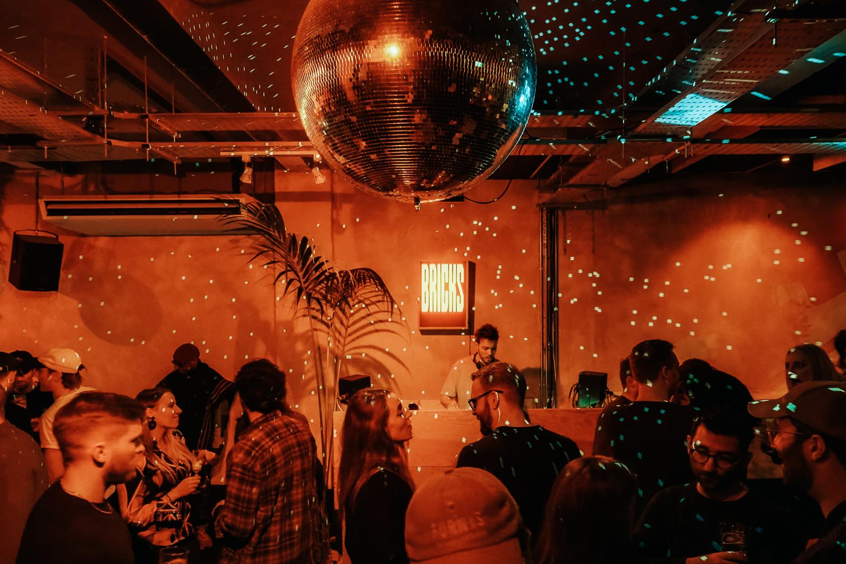 A nightclub event space with a large disco ball, DJ booth, and warm lighting at Bricks.