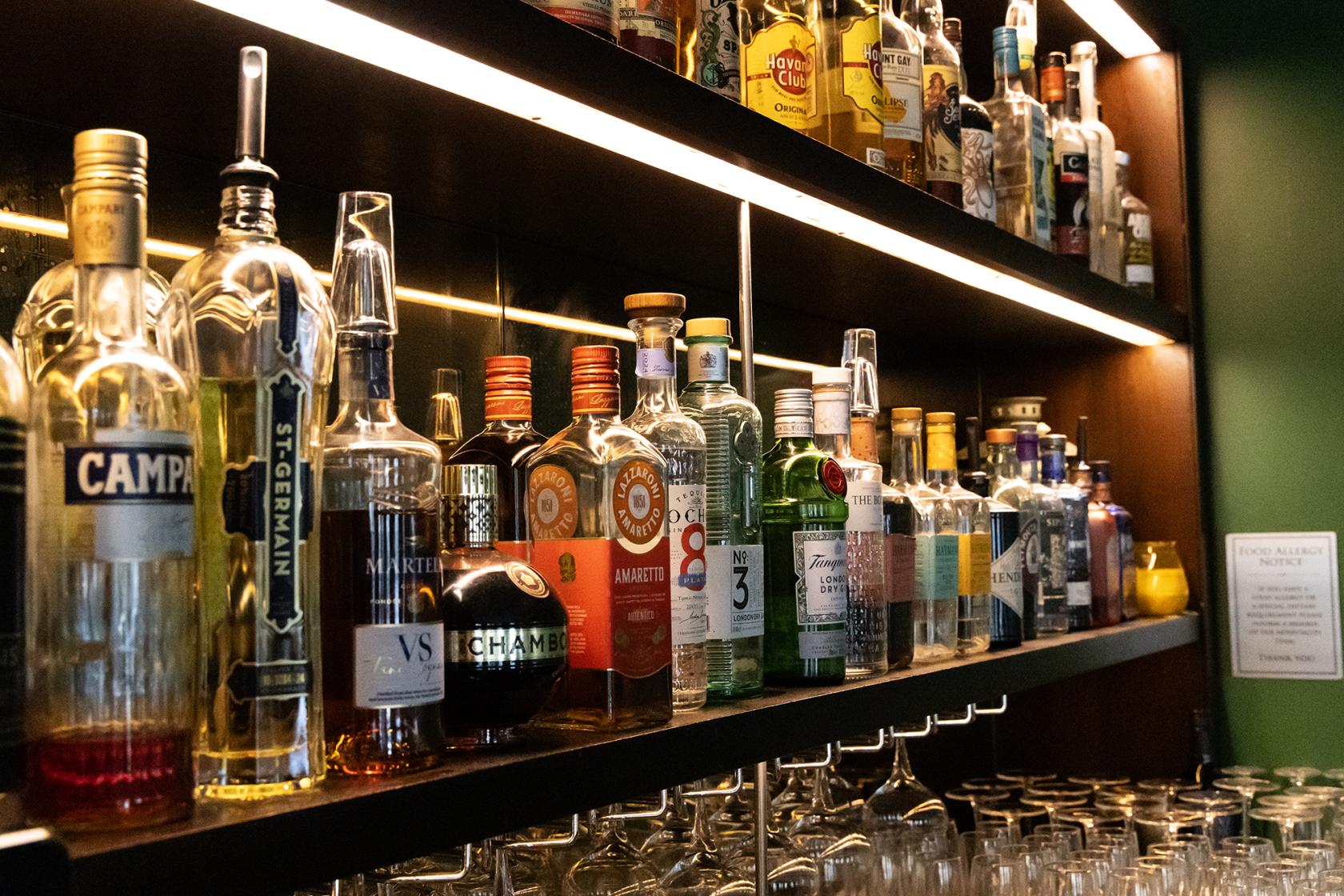 A function room with a backlit bar displaying assorted liquor bottles and hanging glassware at The Maven.