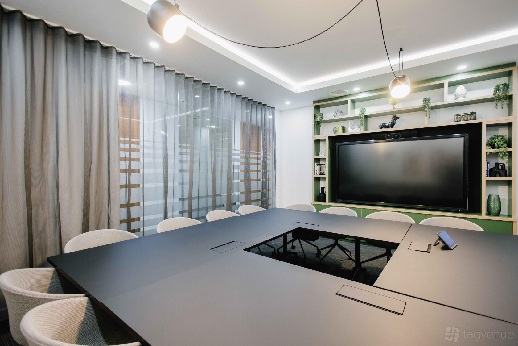 A meeting room with a U-shaped black conference table, built-in shelving, and a large display screen at Orega Gracechurch Street.