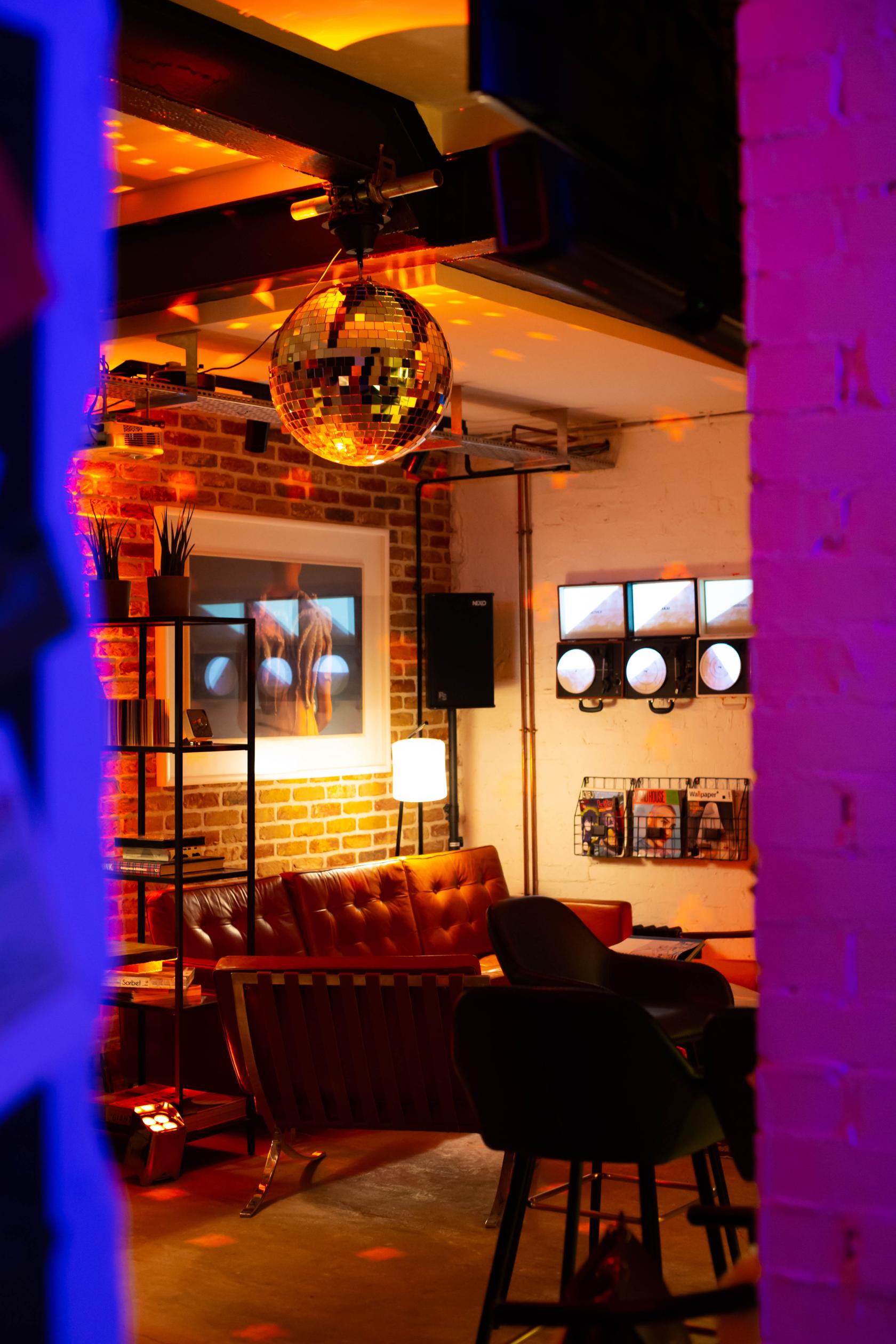 A coworking space with exposed brick walls, leather seating, a disco ball, and wall-mounted art at Jamaica Yard.
