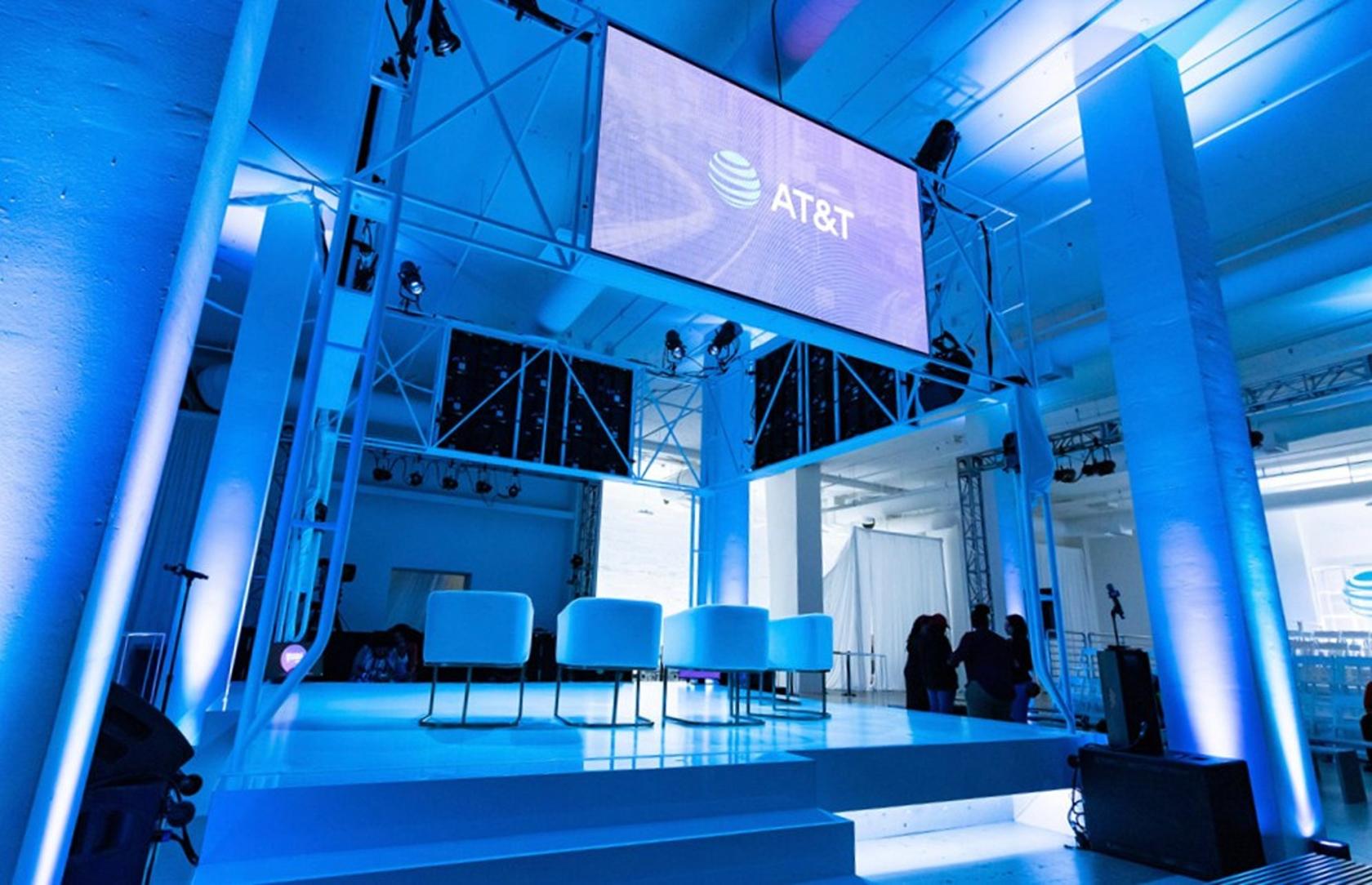 An event venue with a large elevated stage, blue lighting, and modern white chairs at Magic Box LA.